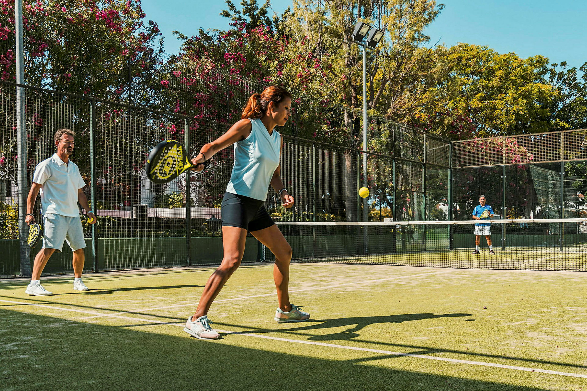 Personer spelar padel på en utomhusbana omgivna av grönska. (AI-genererad text)