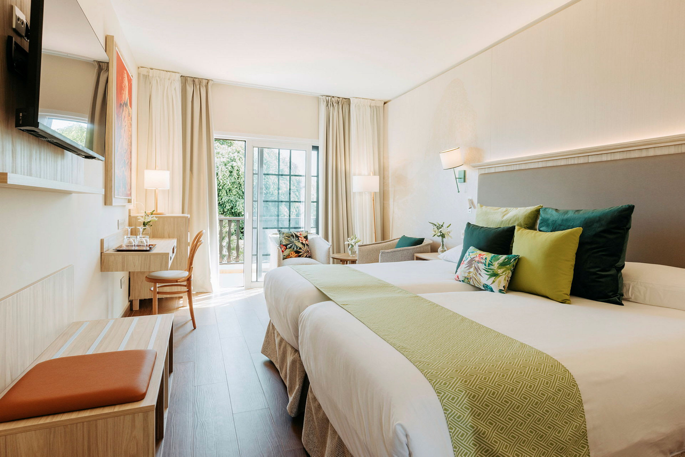 Ett ljust hotellrum med två sängar, prydnadskuddar och en arbetsstation vid balkongen. (AI-genererad text)
