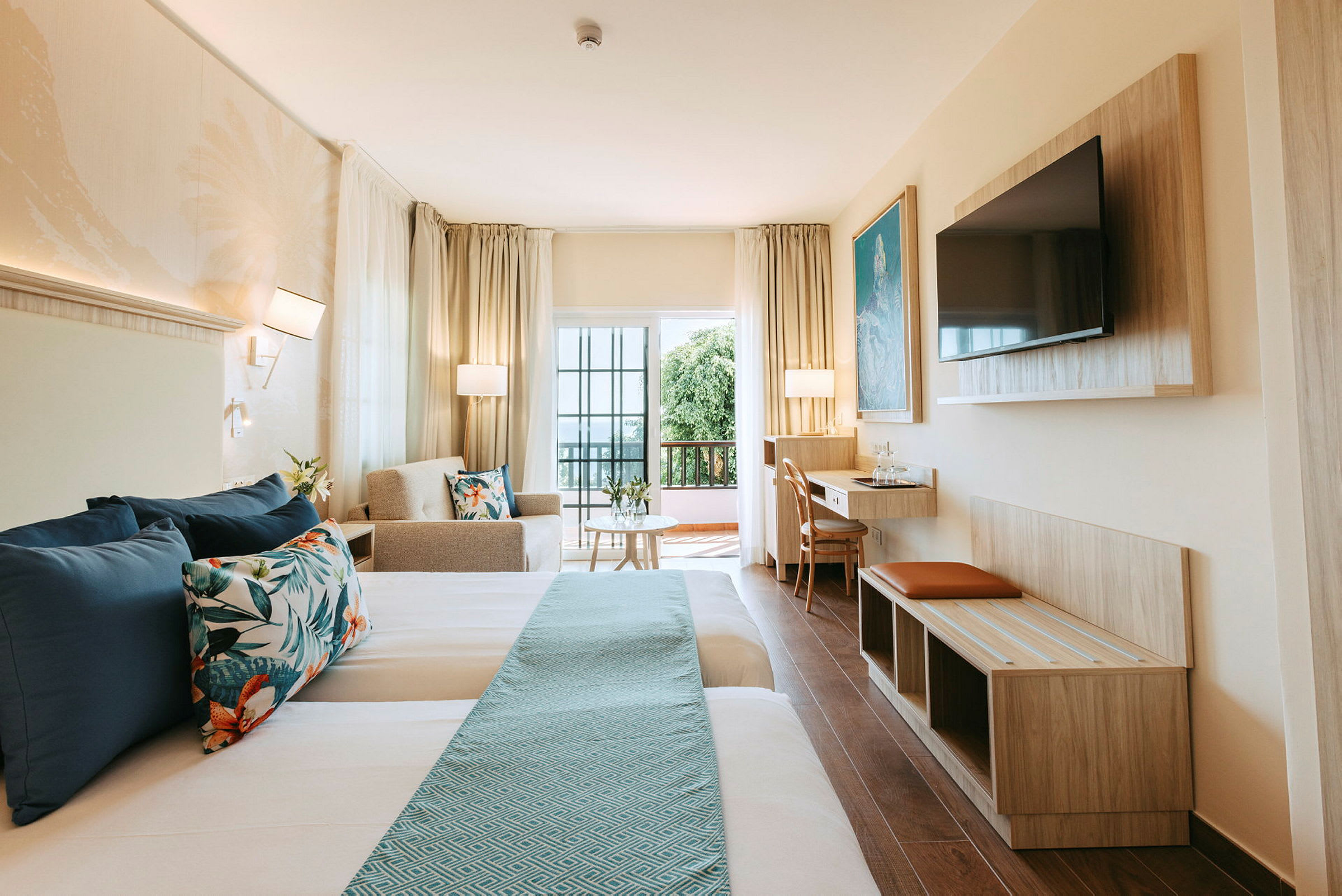Ett hotellrum med två sängar, soffa, bord, och TV, samt en balkong med glasdörrar. (AI-genererad text)