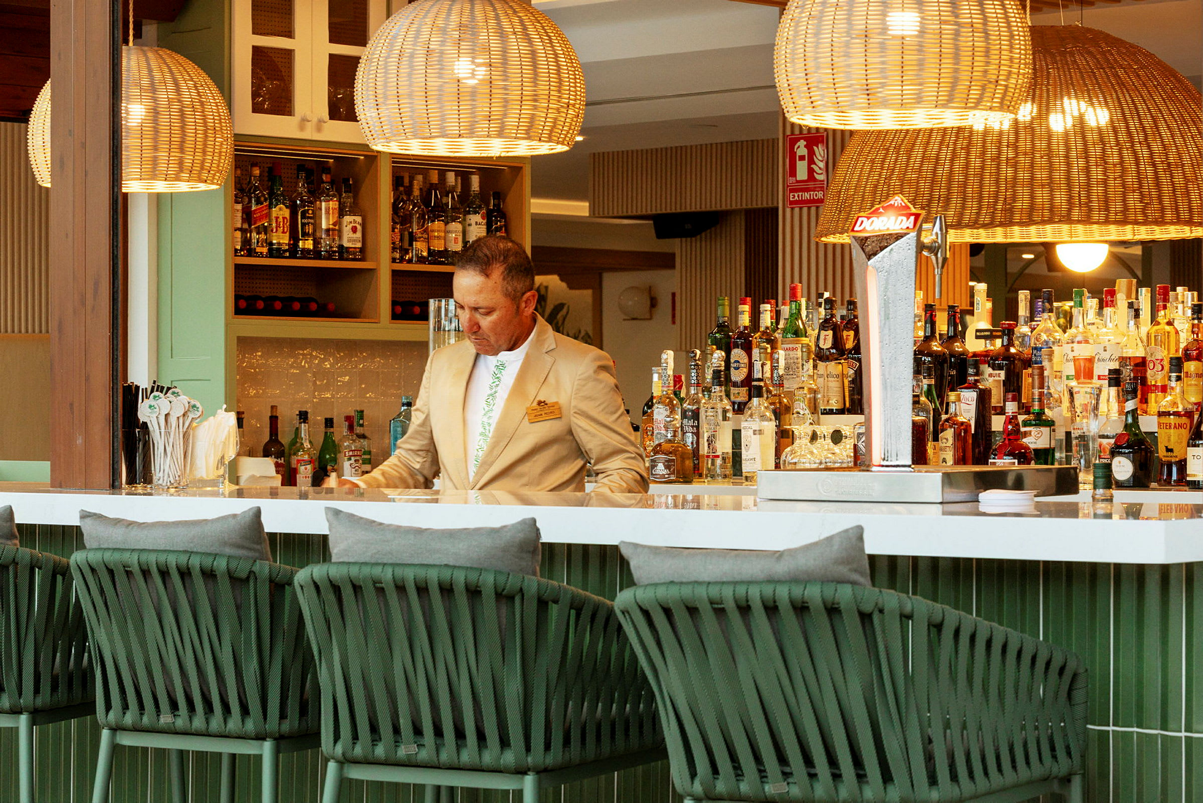 Interiör av en elegant bar med flätade lampor och stolar samt ett sortiment av flaskor och drycker på hyllorna. (AI-genererad text)