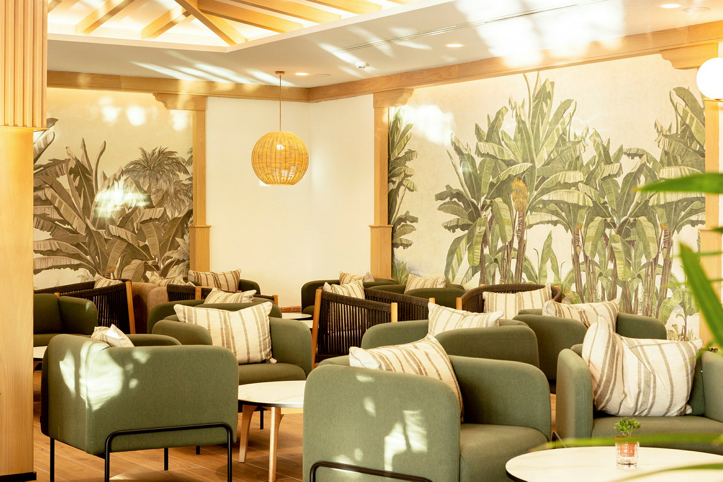 En elegant lounge med gröna fåtöljer, randiga kuddar och väggar prydda med växtmotiv. (AI-genererad text)