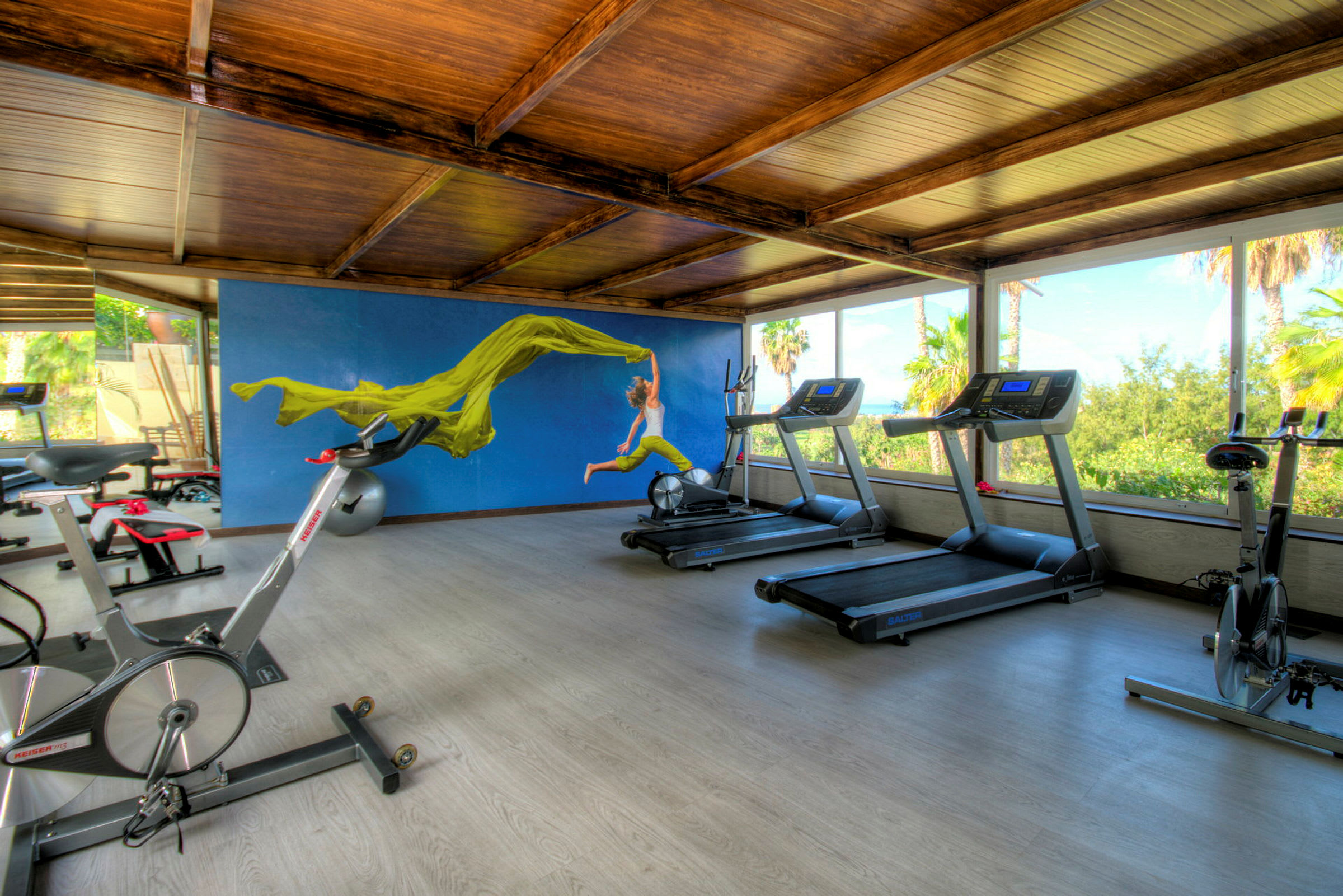 Ett gym med träningsutrustning och en blå vägg med en bild av en person med en grön flagga. (AI-genererad text)