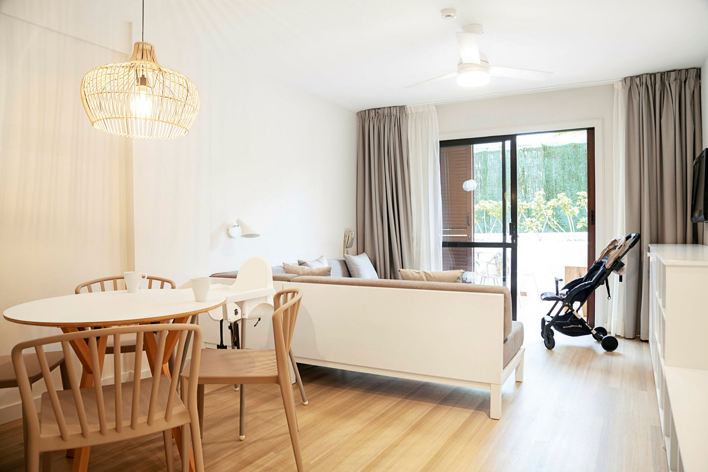 Ett ljust och modernt inrett vardagsrum med ett matbord, en soffa och en barnvagn vid glasdörren. (AI-genererad text)