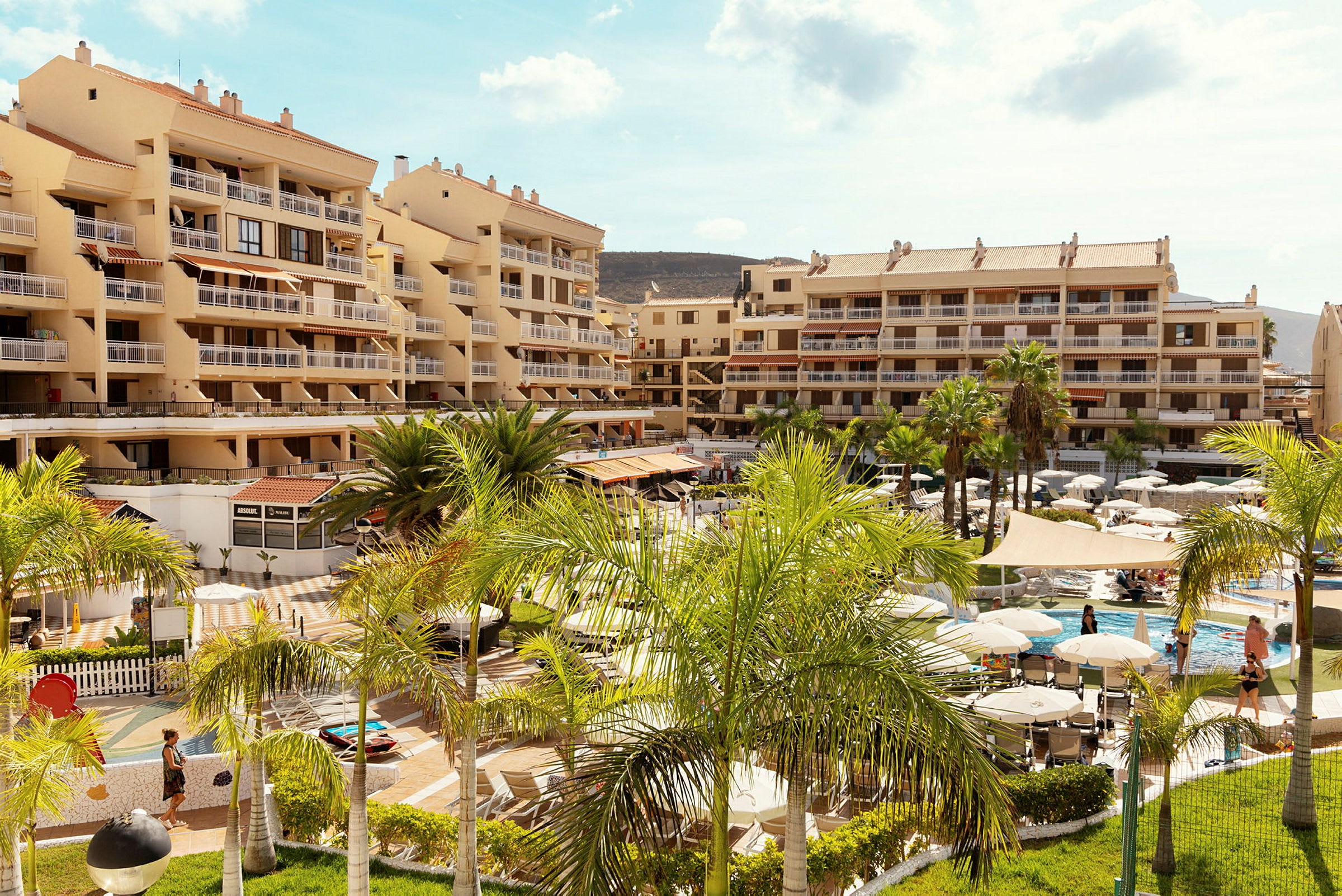 Hotellområde med pooler, parasoller och byggnader i bakgrunden. (AI-genererad text)