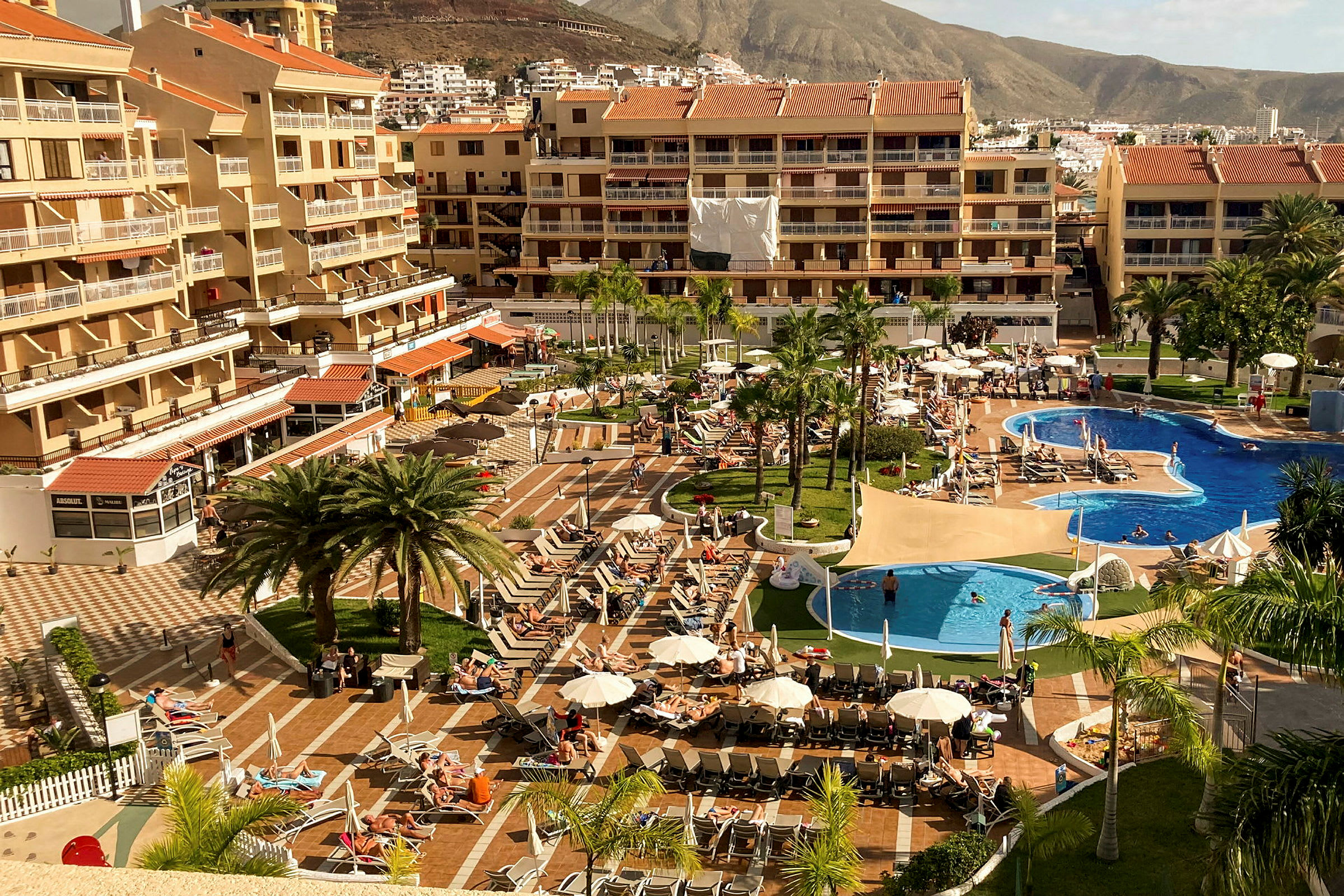 Hotellområde med pooler, solstolar och byggnader i bakgrunden. (AI-genererad text)