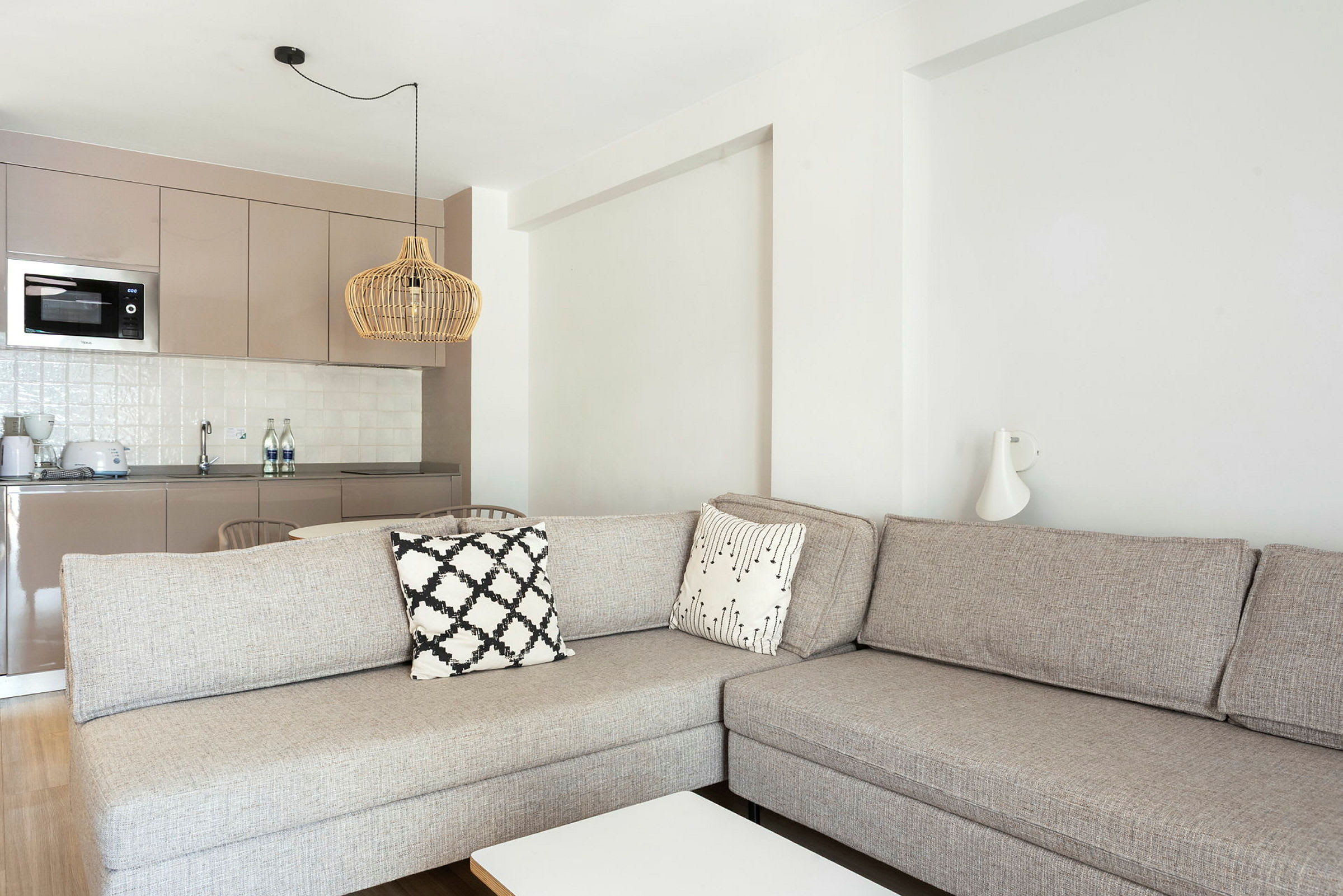 Ett vardagsrum med en beige soffa och köksdel i bakgrunden. (AI-genererad text)