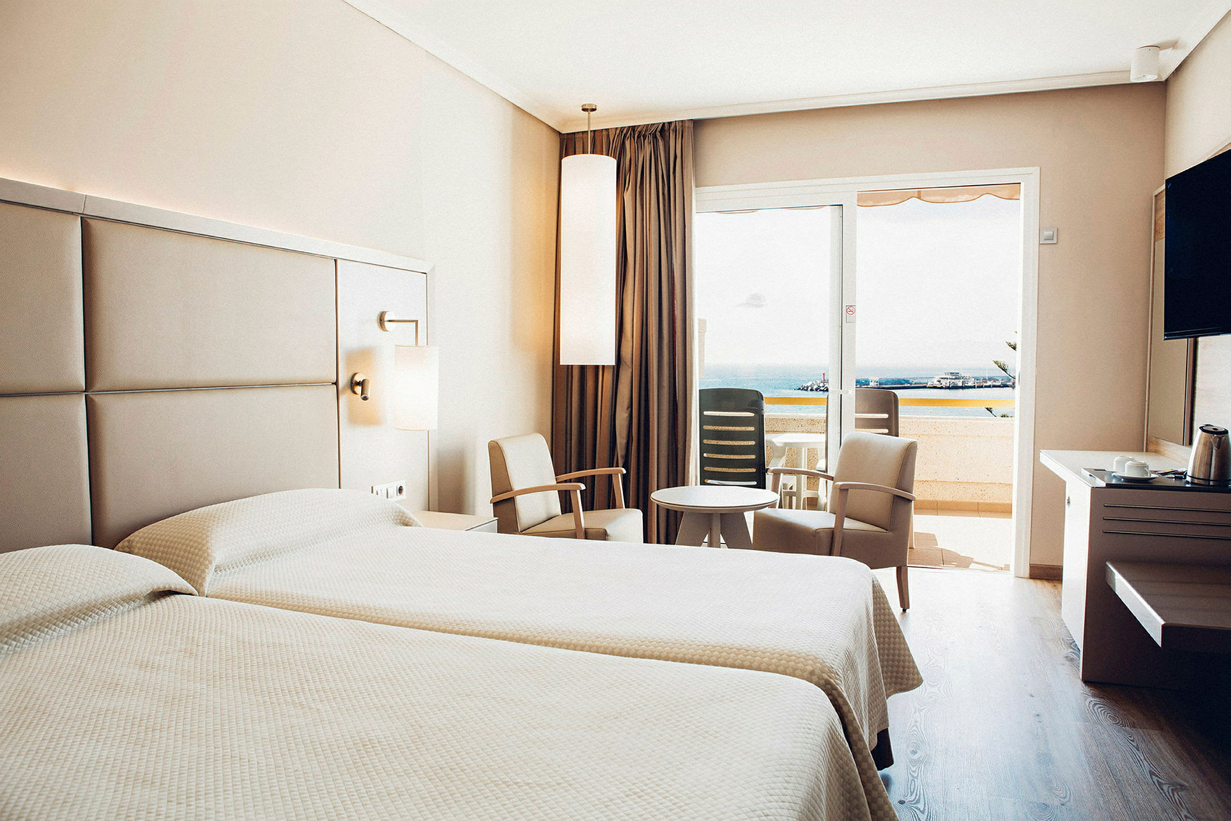 Hotellrum med två sängar, sittgrupp och balkong med utsikt. (AI-genererad text)
