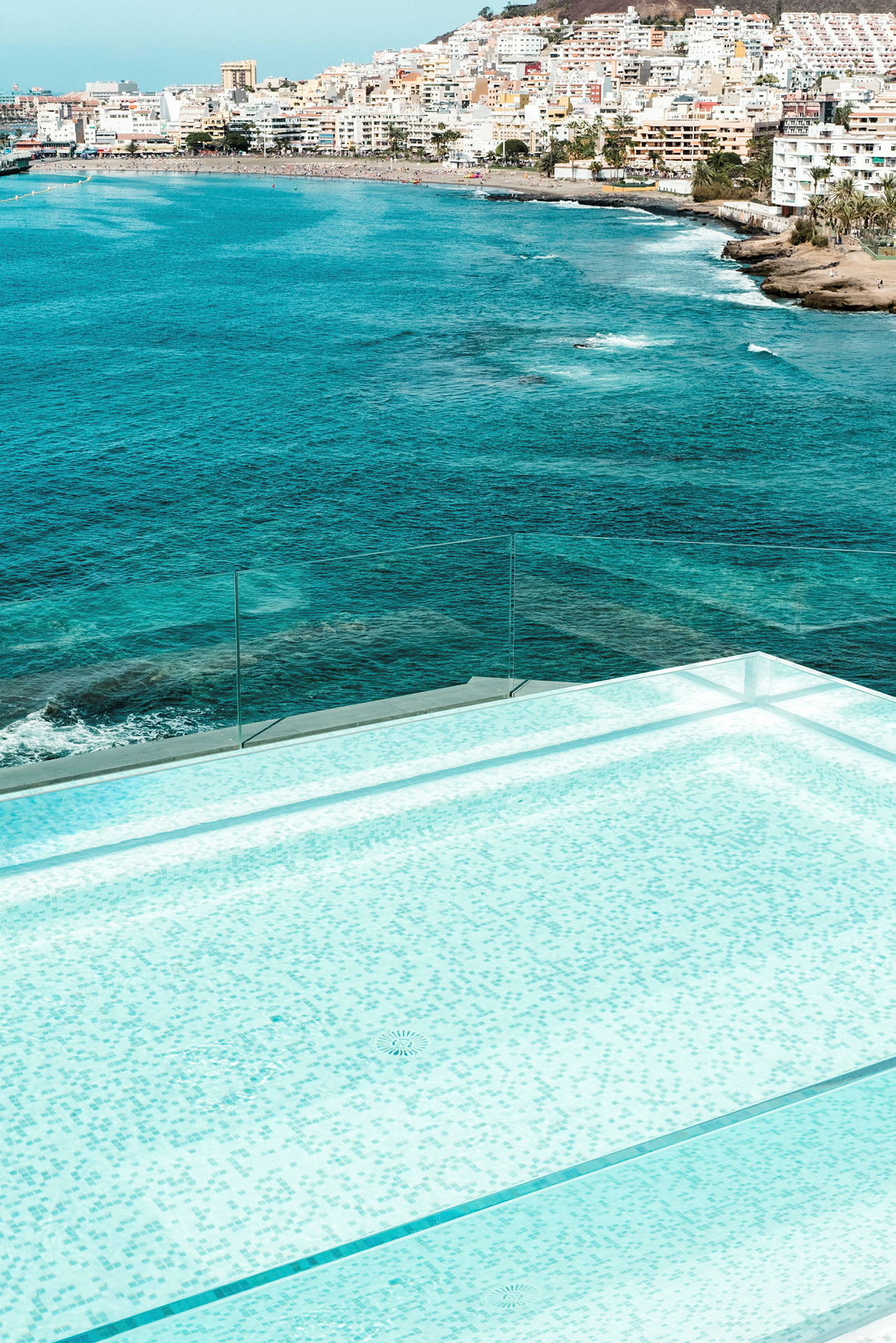 En modern infinitypool med utsikt över havet och en stadsstrand. (AI-genererad text)