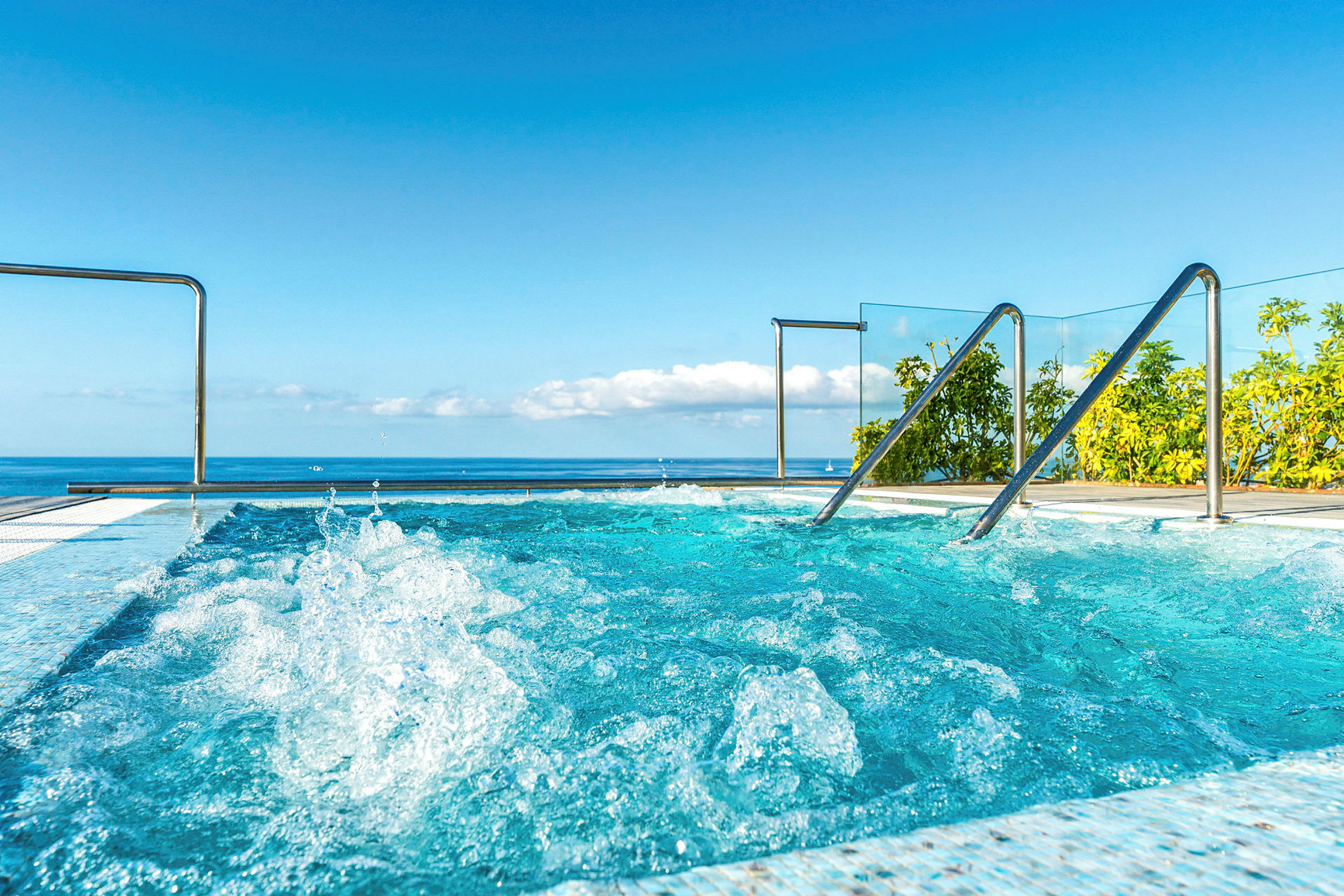 Utsikt över ett turkost bubbelpool med havet och himlen i bakgrunden. (AI-genererad text)