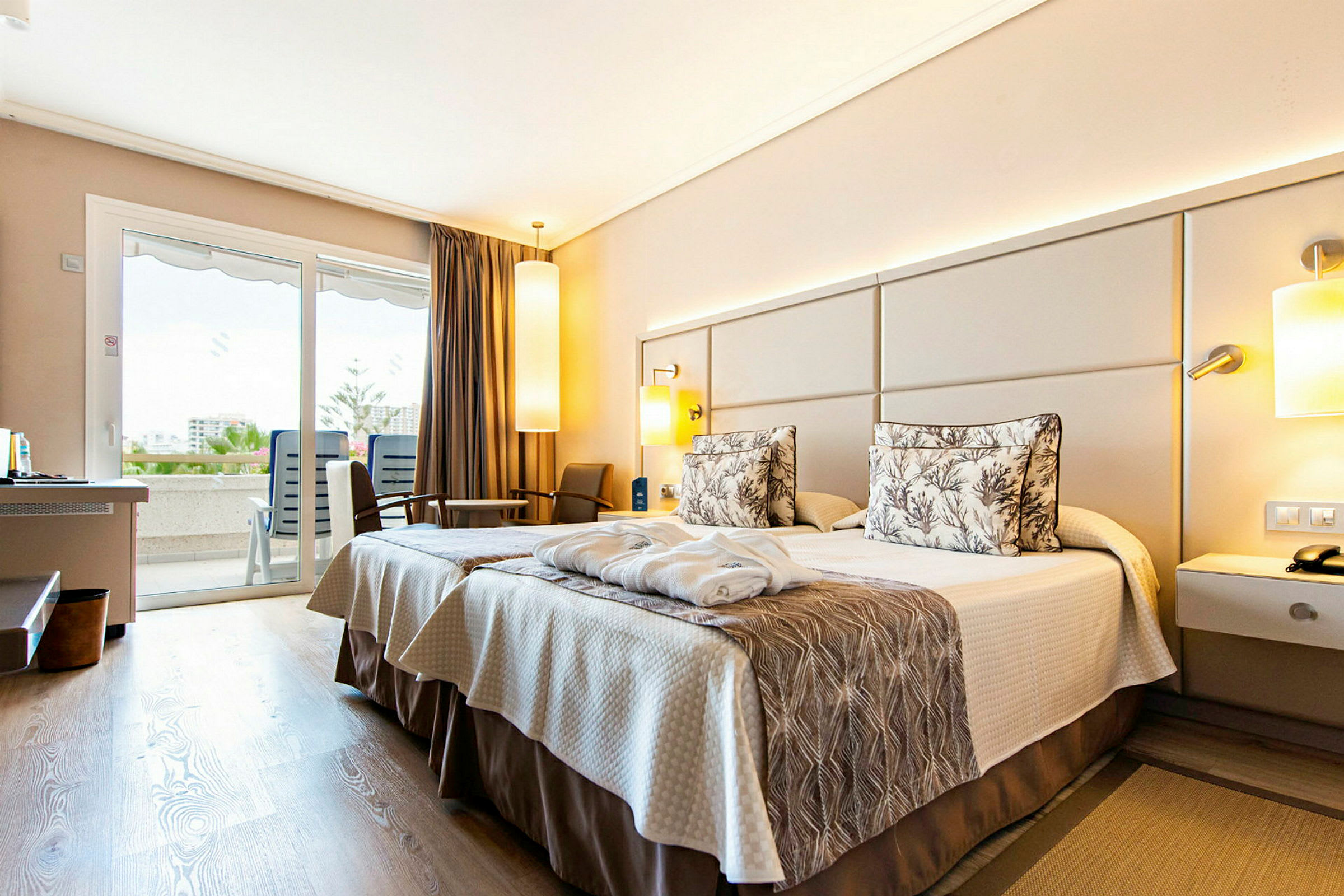 Hotellrum med två sängar och inredning i neutrala toner. Utsikt mot balkong genom glasdörrar. (AI-genererad text)