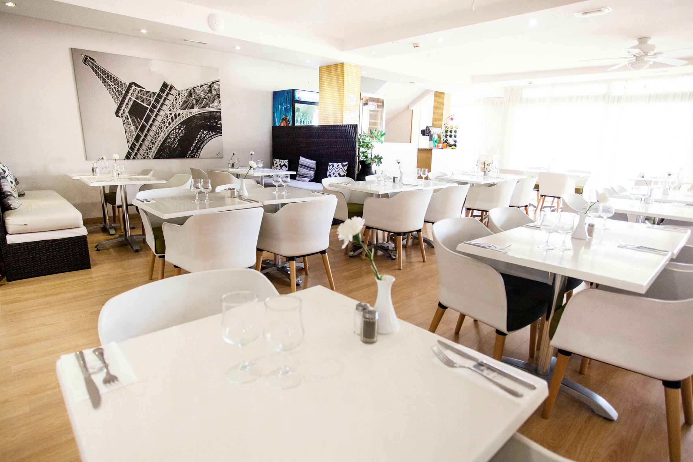 Ett ljust inrett restaurangområde med vita bord och stolar. (AI-genererad text)