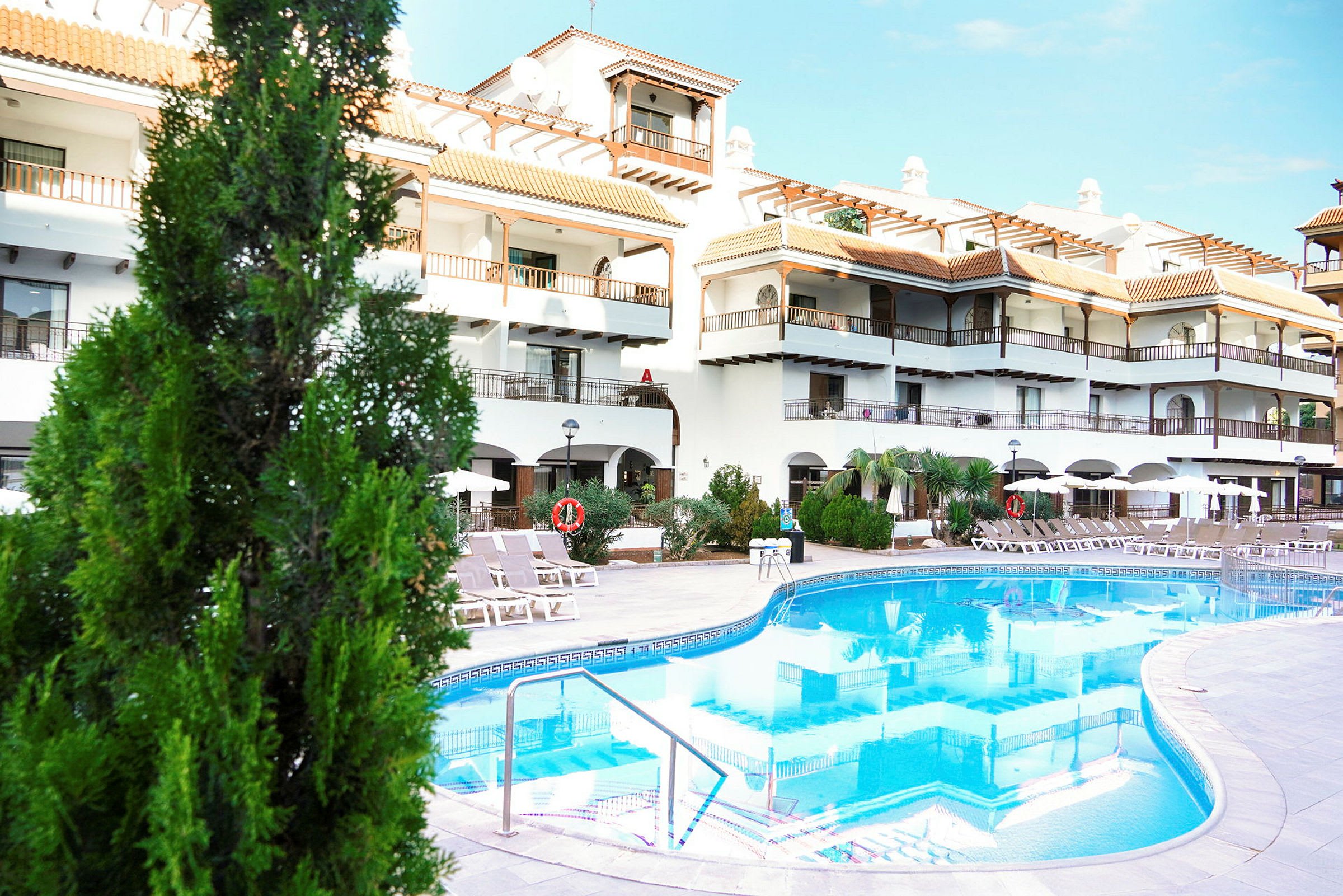 Hotellbyggnad med pool framför och solstolar. (AI-genererad text)