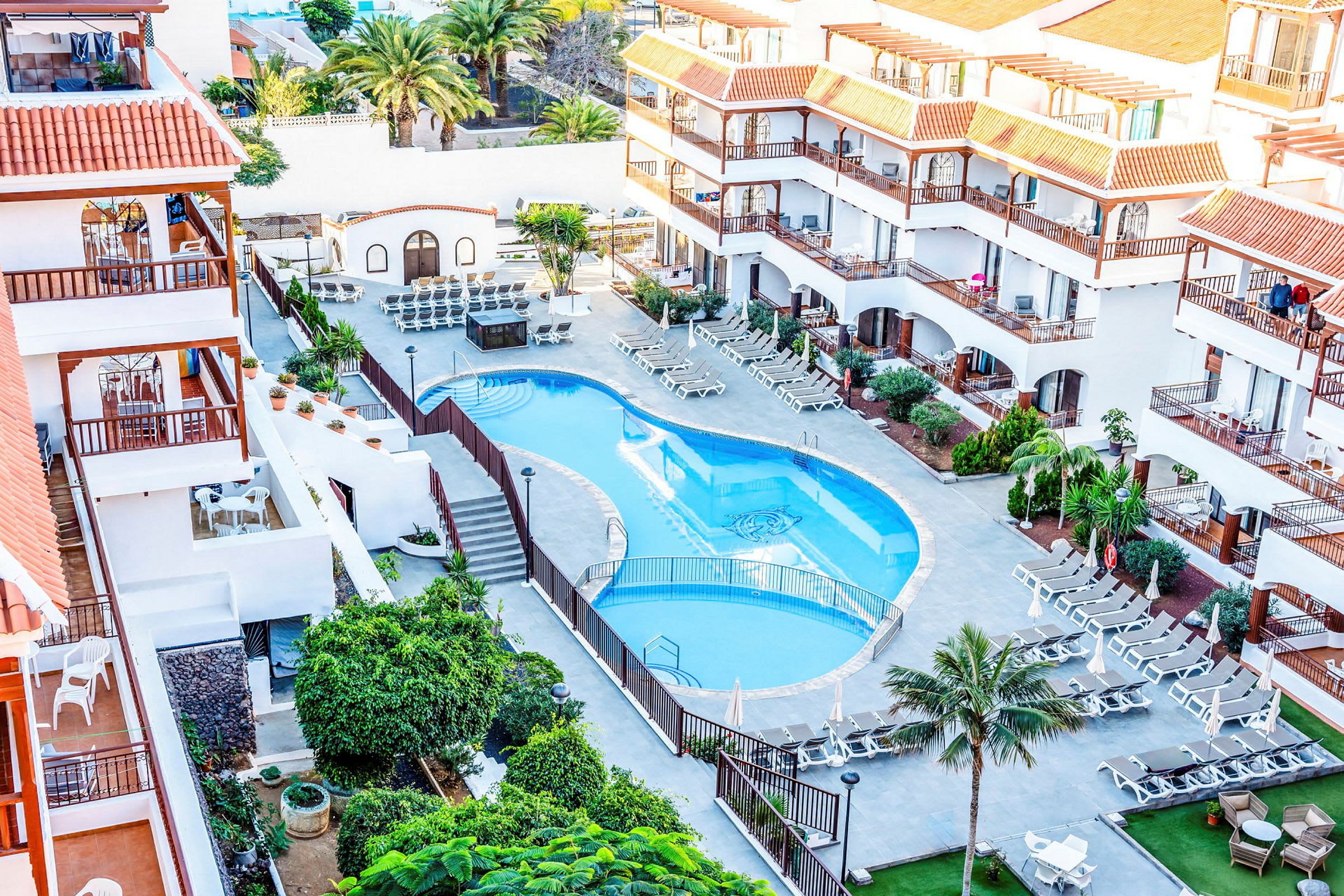 Hotellets poolområde med solstolar och omgivande byggnader. (AI-genererad text)