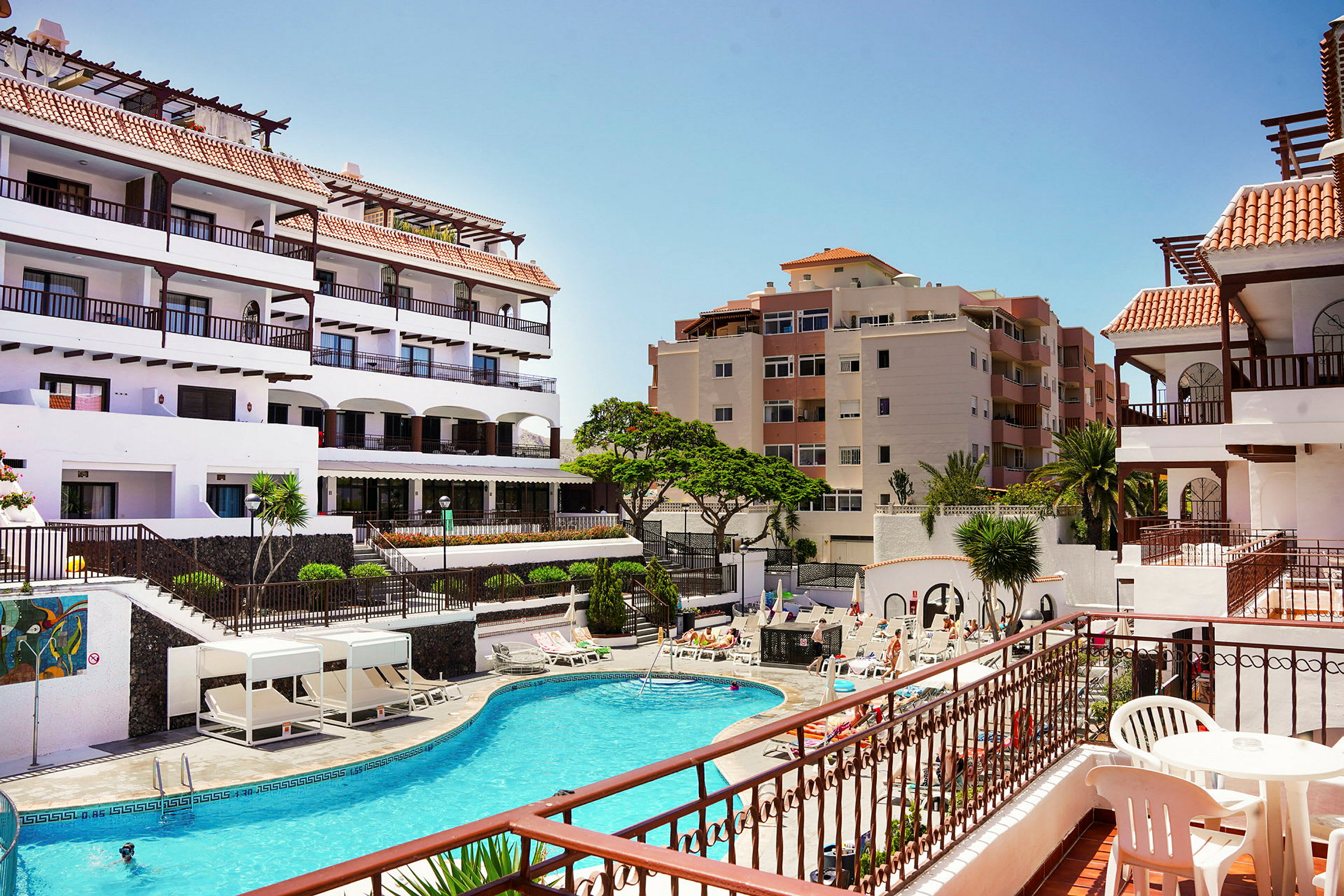 Bild av en hotellanläggning med en pool och solstolar, omgiven av flerbostadshus. (AI-genererad text)