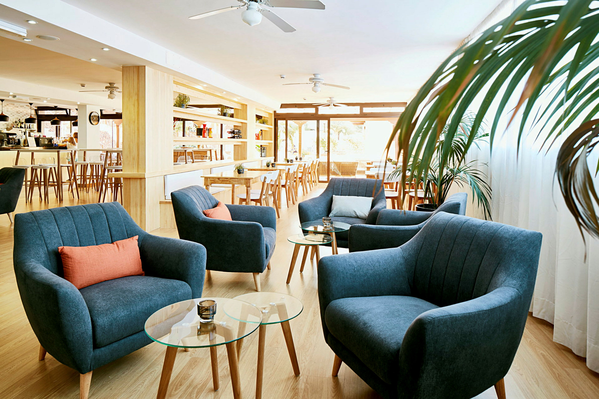 En ljus loungemiljö med blå fåtöljer, orange kuddar och glasbord. (AI-genererad text)