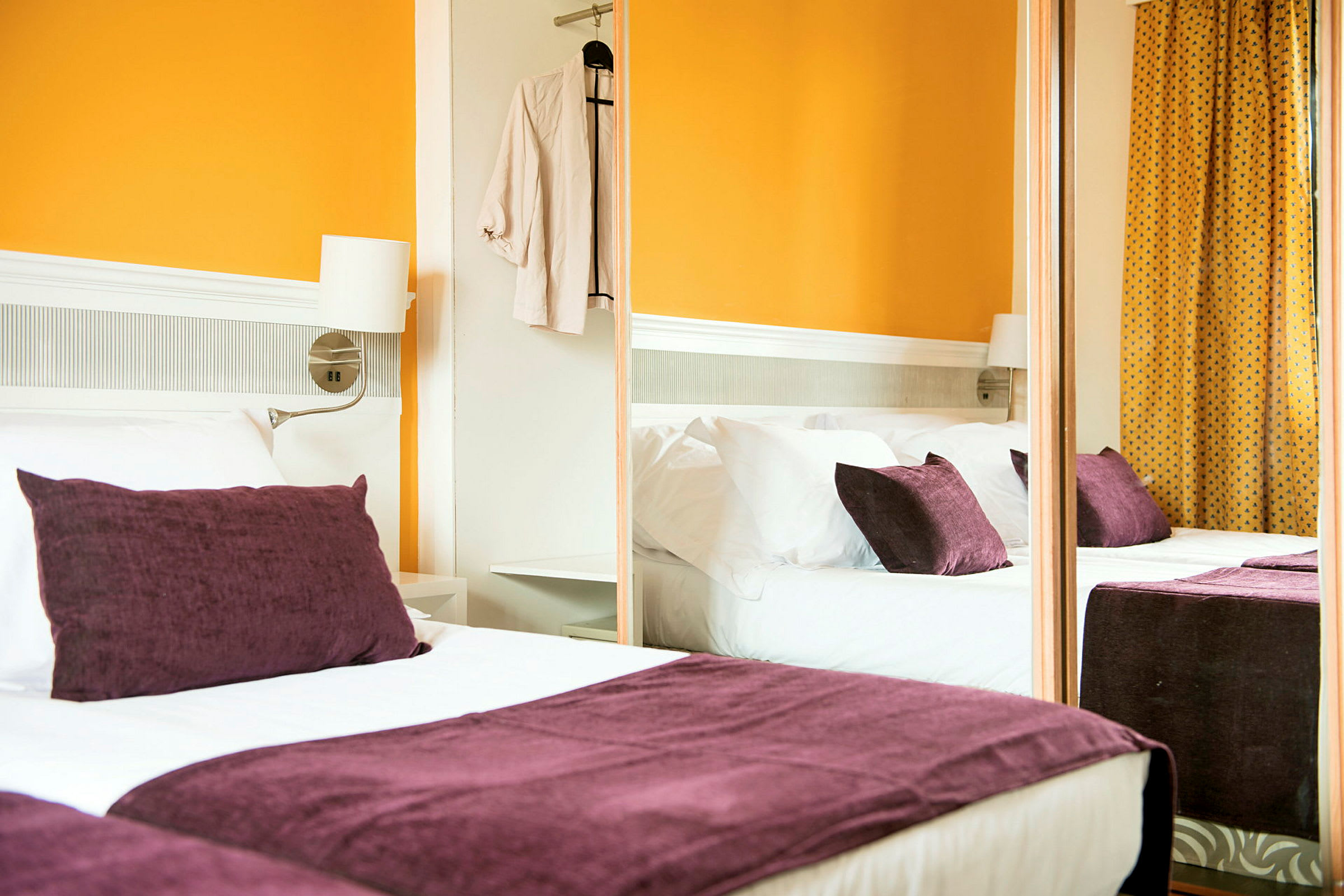 Ett hotellrum med en dubbelsäng, lila kuddar och orange väggar. (AI-genererad text)