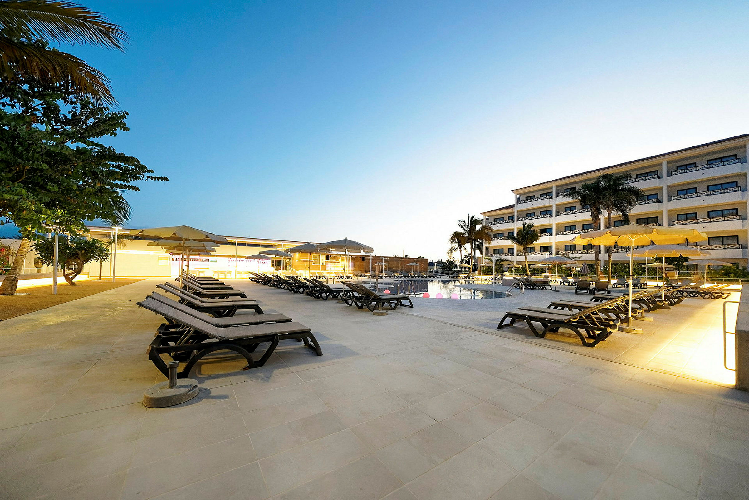 Bild på en pool med solstolar och parasoller vid ett hotell. (AI-genererad text)