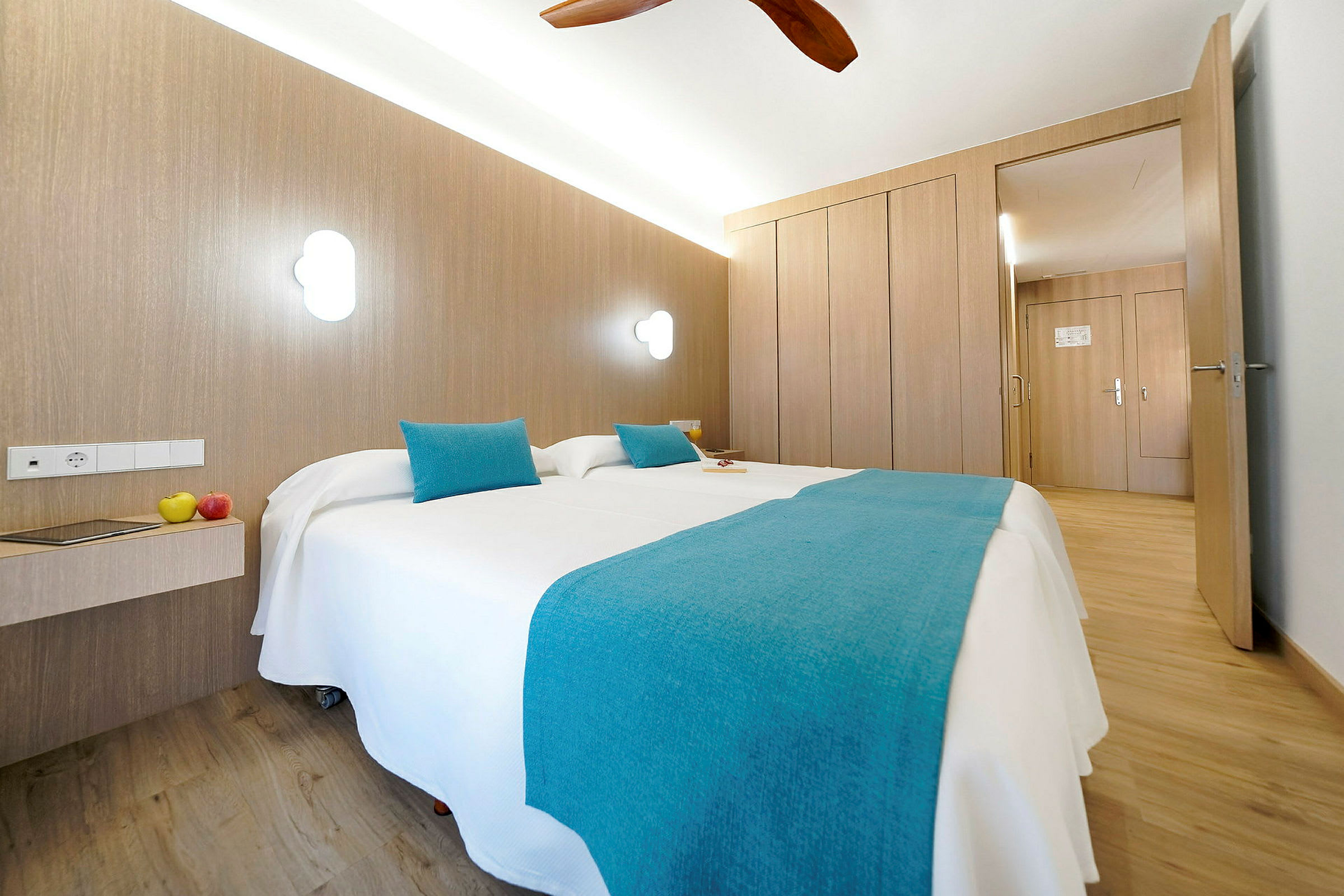 Ett hotellrum med ljus inredning, två enkelsängar med blå överkast och kuddar. (AI-genererad text)