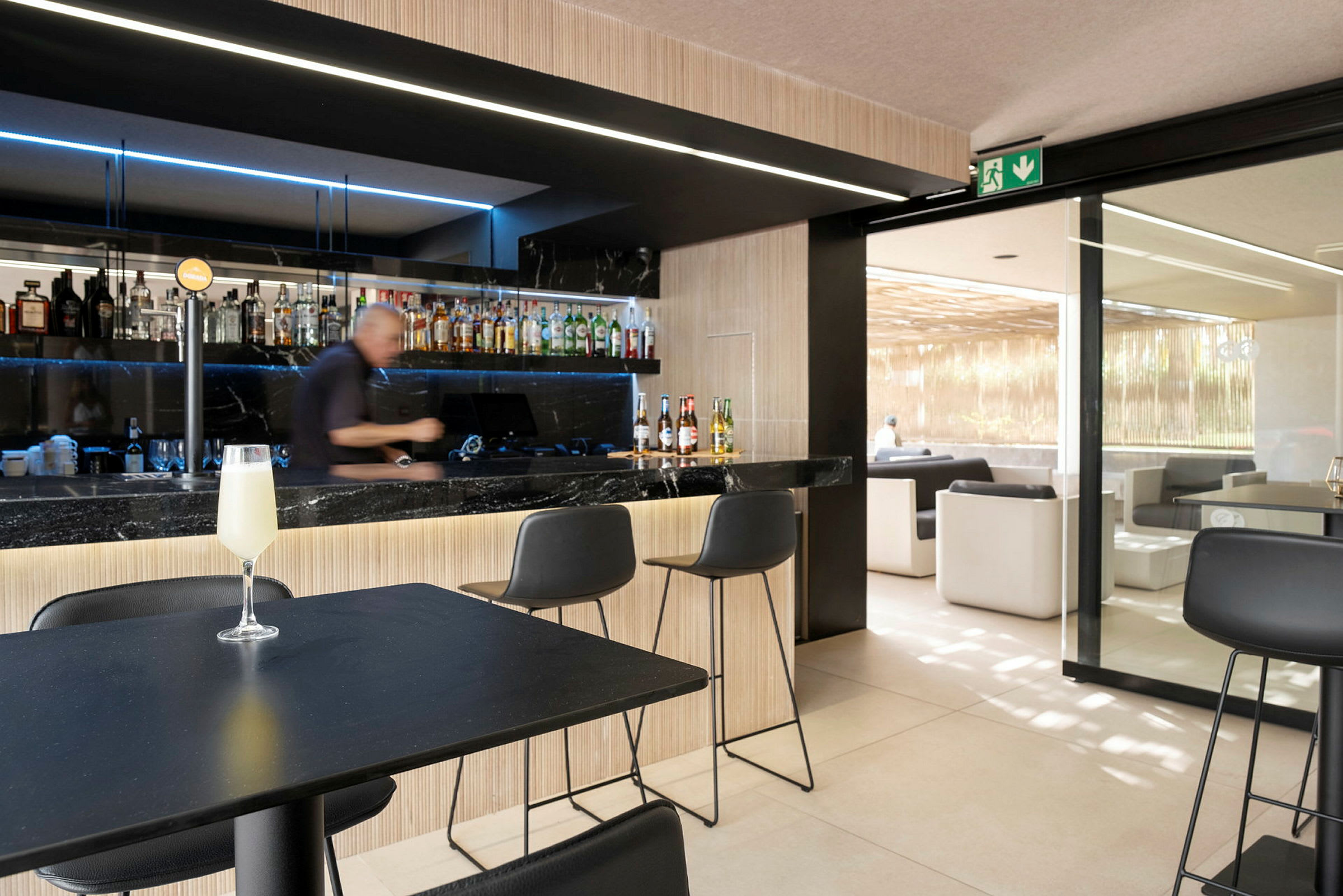 En bild av en bar med en bartender som förbereder drycker. Framför honom står stolar, och en pärlande drink är placerad på ett bord. (AI-genererad text)