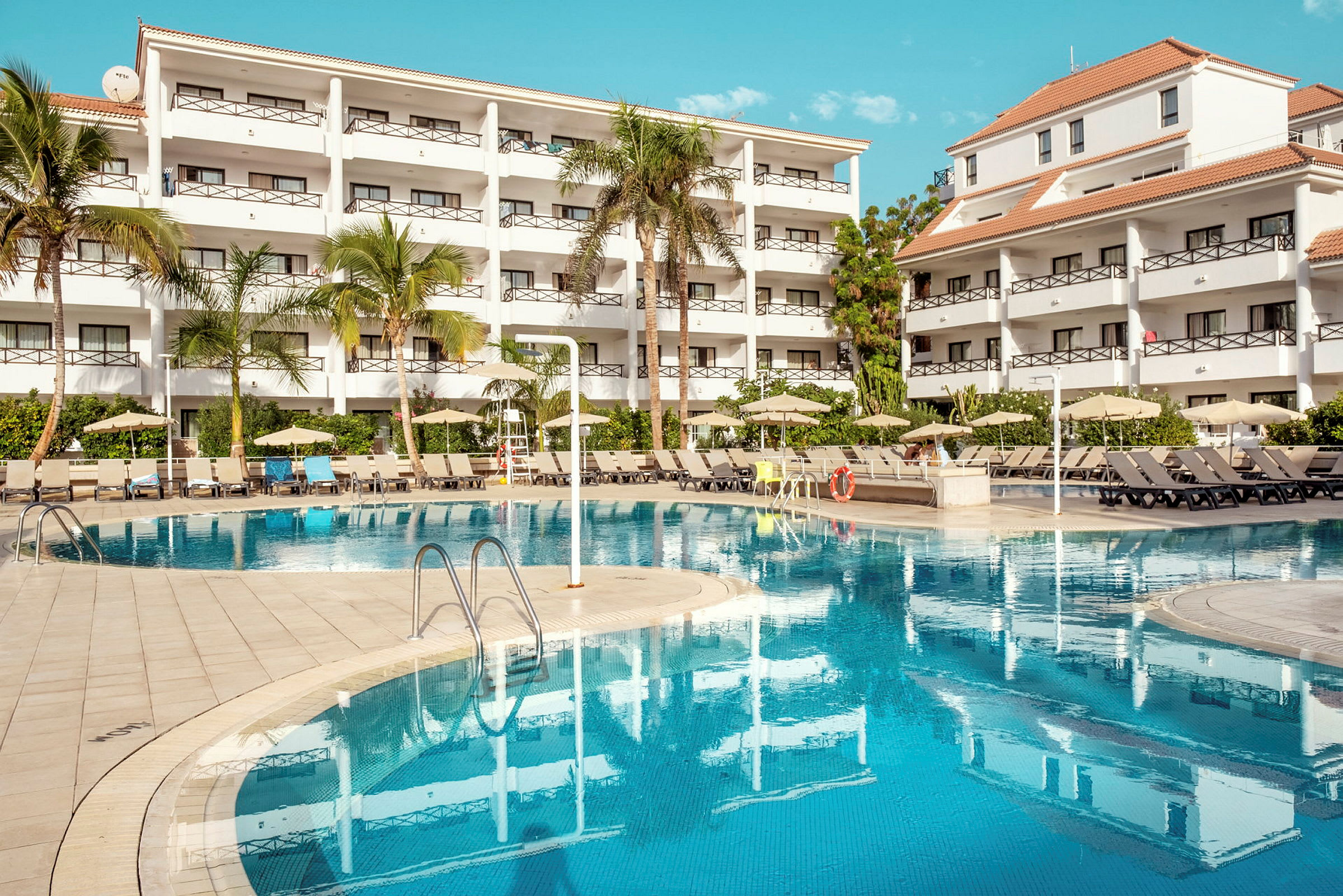 Bild av ett hotellkomplex med vita byggnader, träd och en pool. (AI-genererad text)