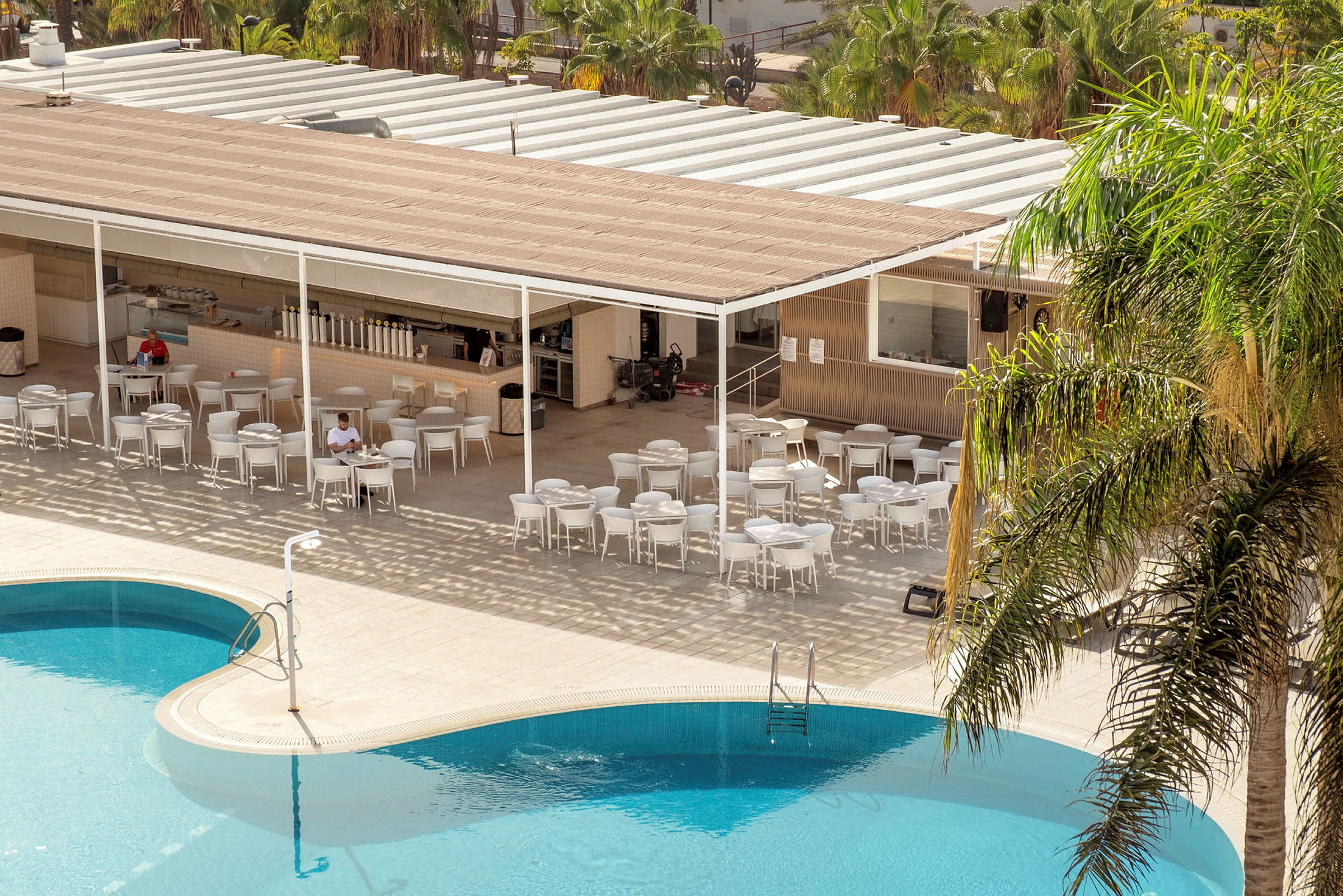 Bild på en pool och en sittgrupp vid en bar med skuggtak. (AI-genererad text)