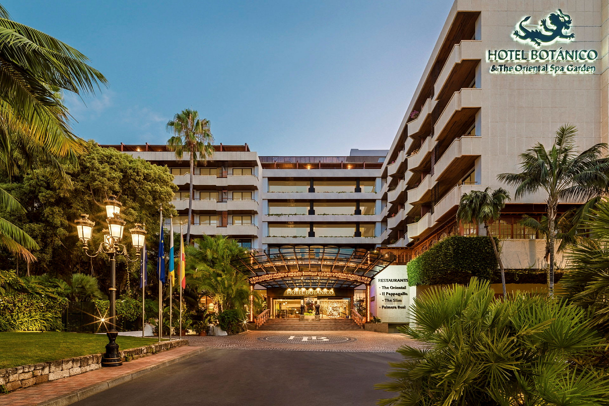 Ingången till Hotel Botanico, omgivet av tropiska växter och belyst av gatlampor. (AI-genererad text)
