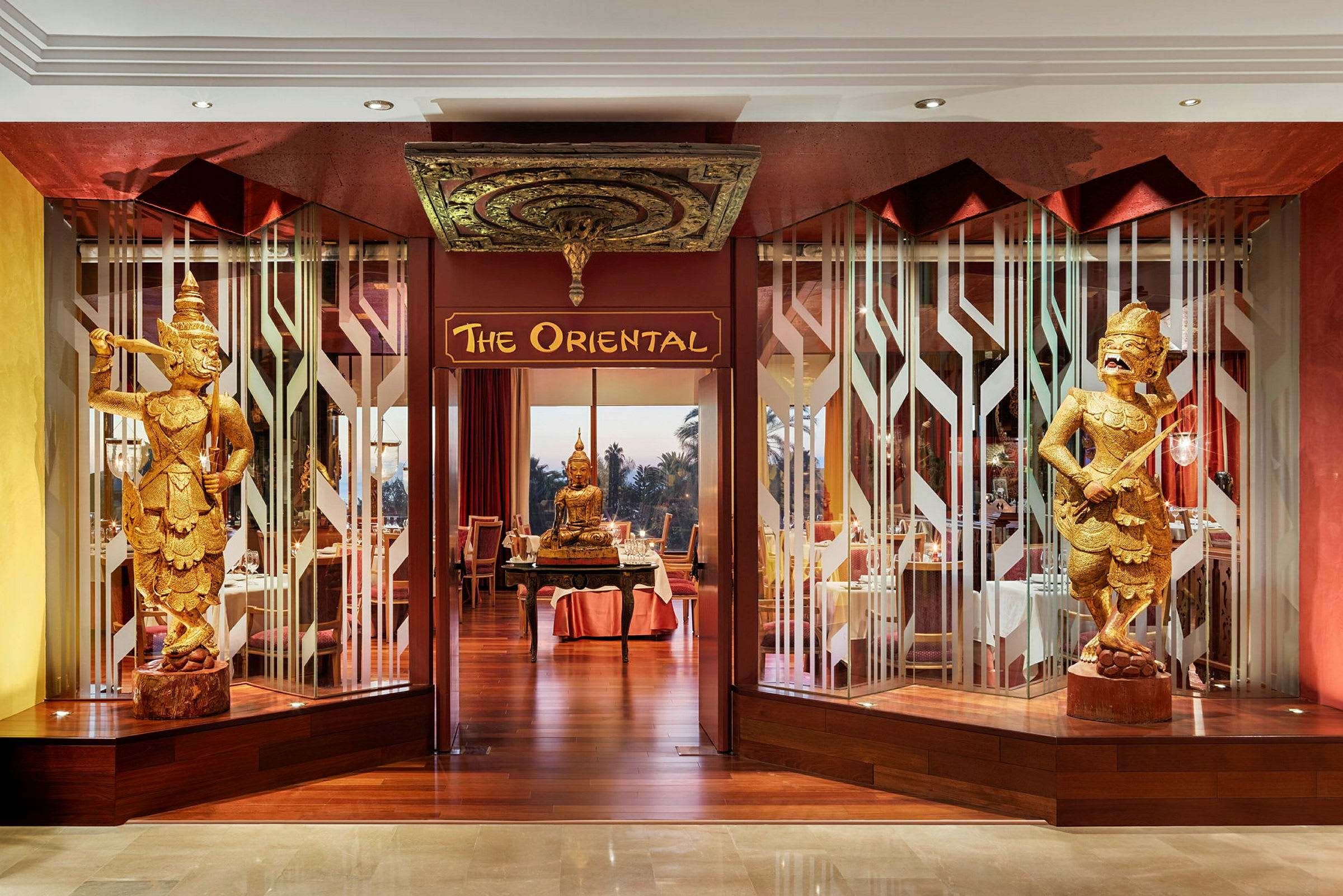 Ingången till restaurangen 'The Oriental' med dekorativa gyllene figurer och en Buddha-staty. (AI-genererad text)