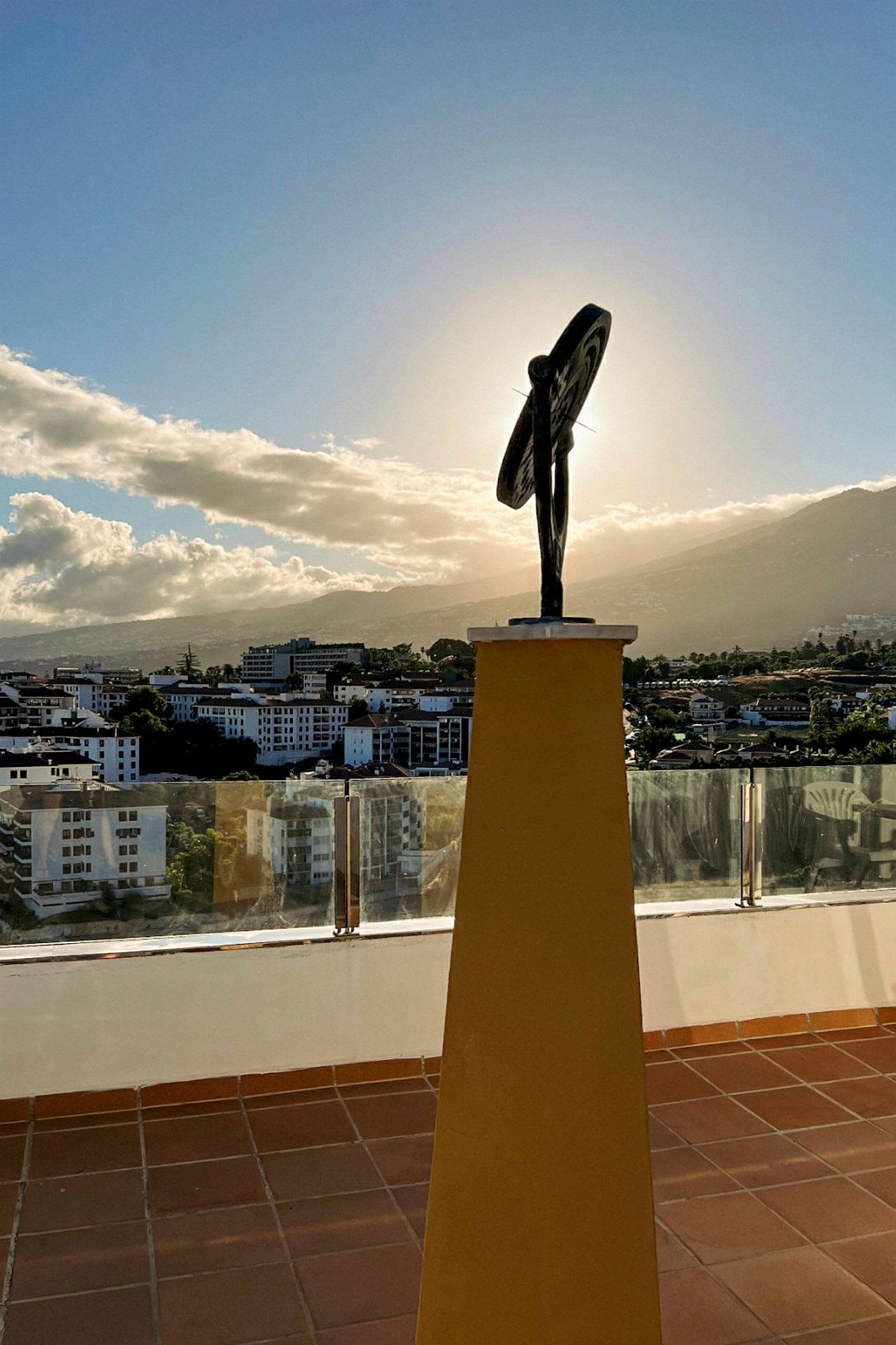 En skulptur på en gul piedestal med en stad och berg i bakgrunden. (AI-genererad text)