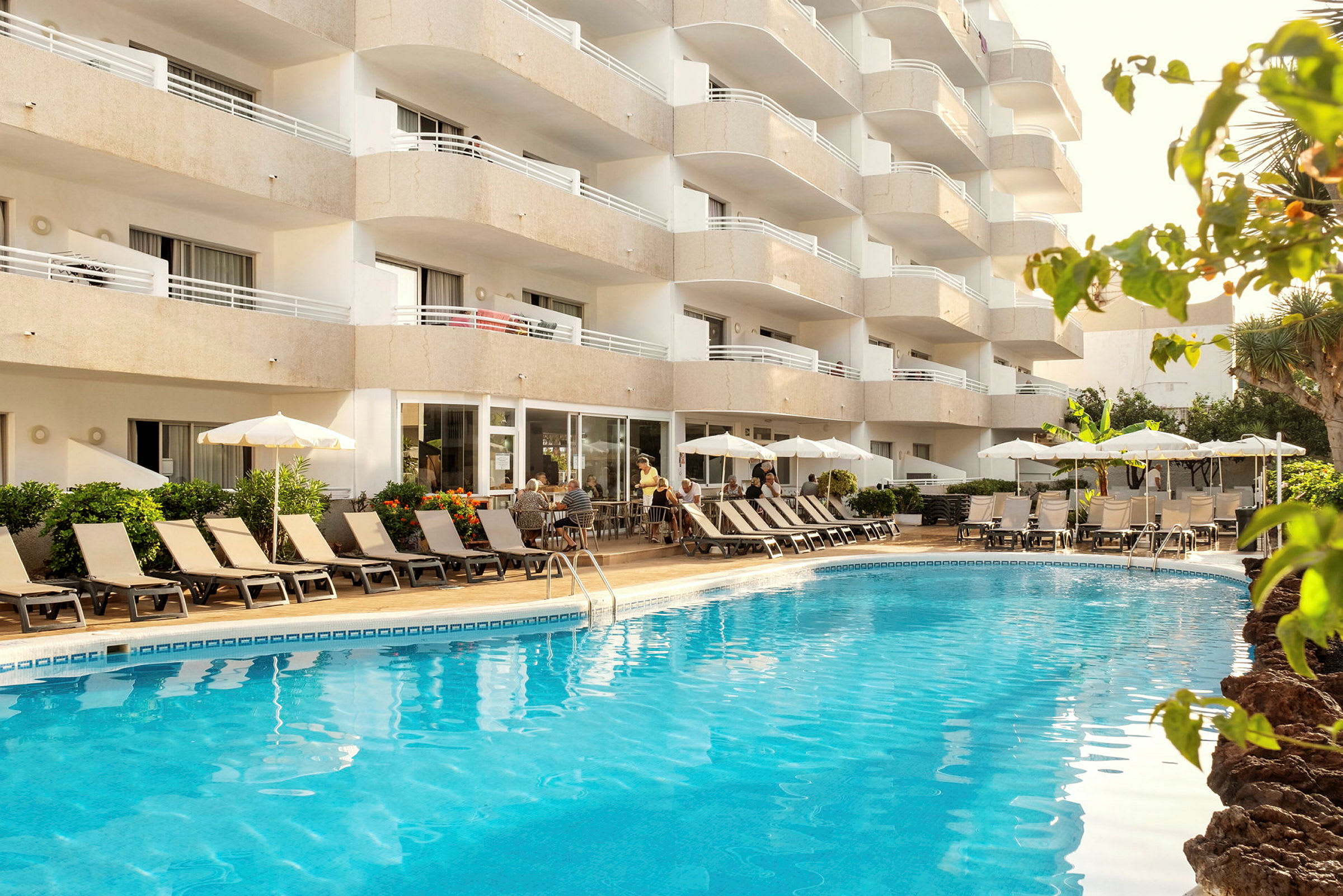 Bild av ett hotell med balkonger, pool och solstolar. (AI-genererad text)
