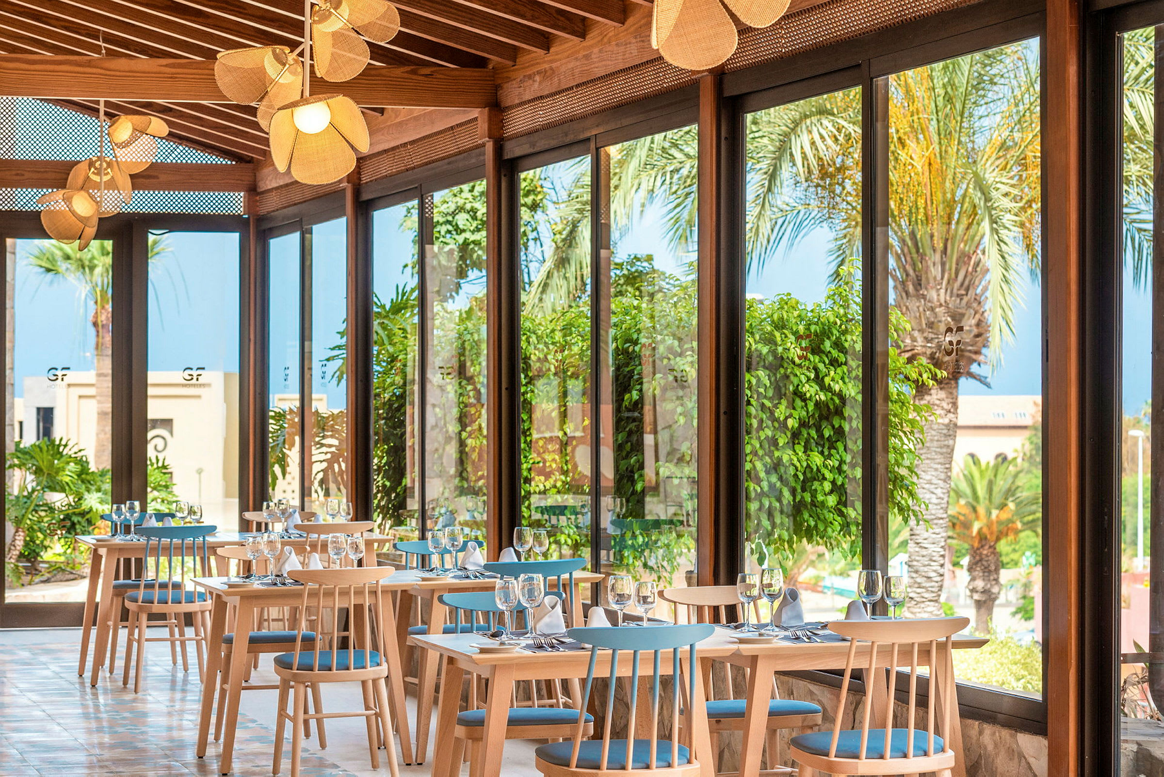 En restaurang med stora fönster och utsikt över palmer och växter. (AI-genererad text)