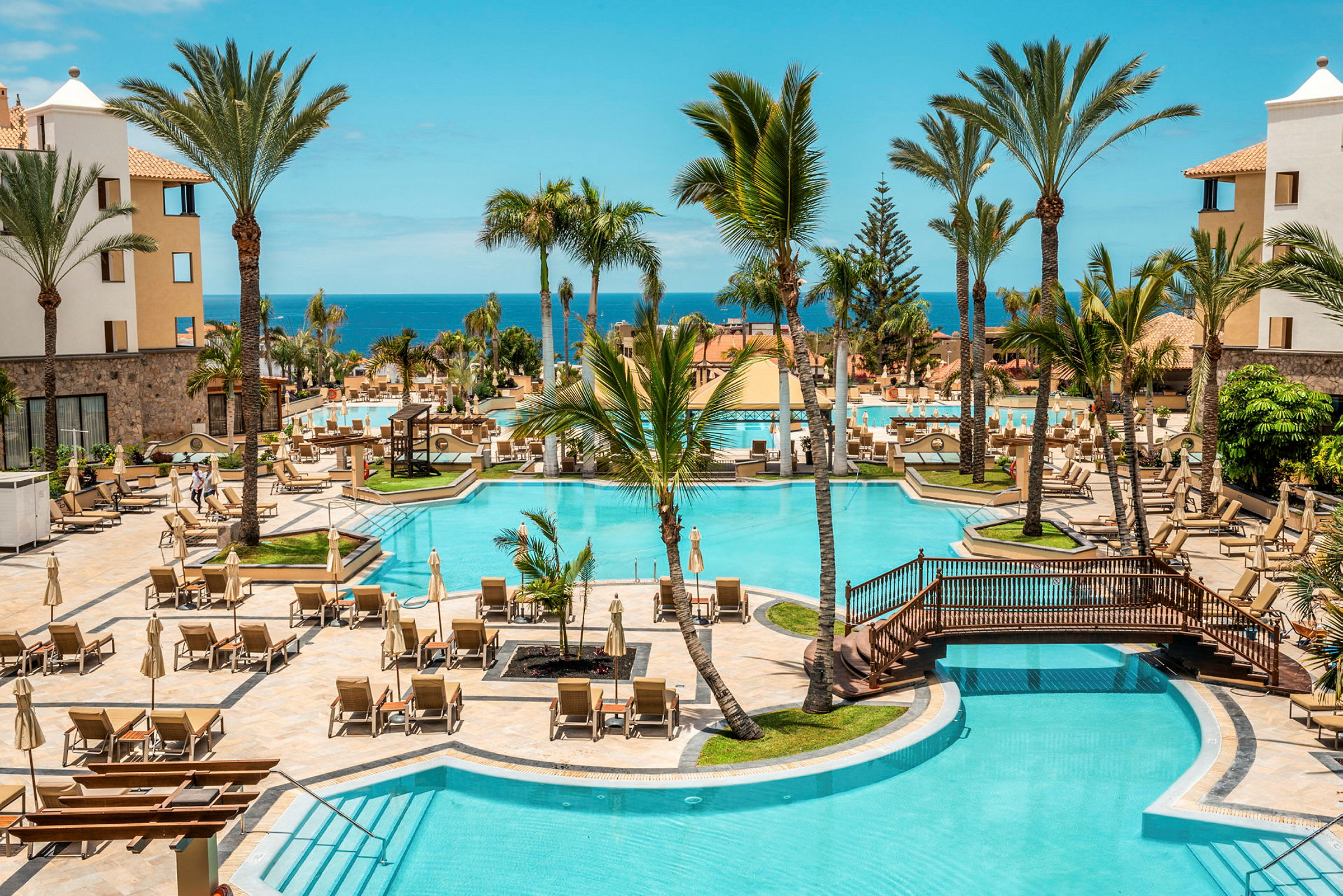 Hotellpoolområde med solstolar, palmer och havsutsikt. (AI-genererad text)