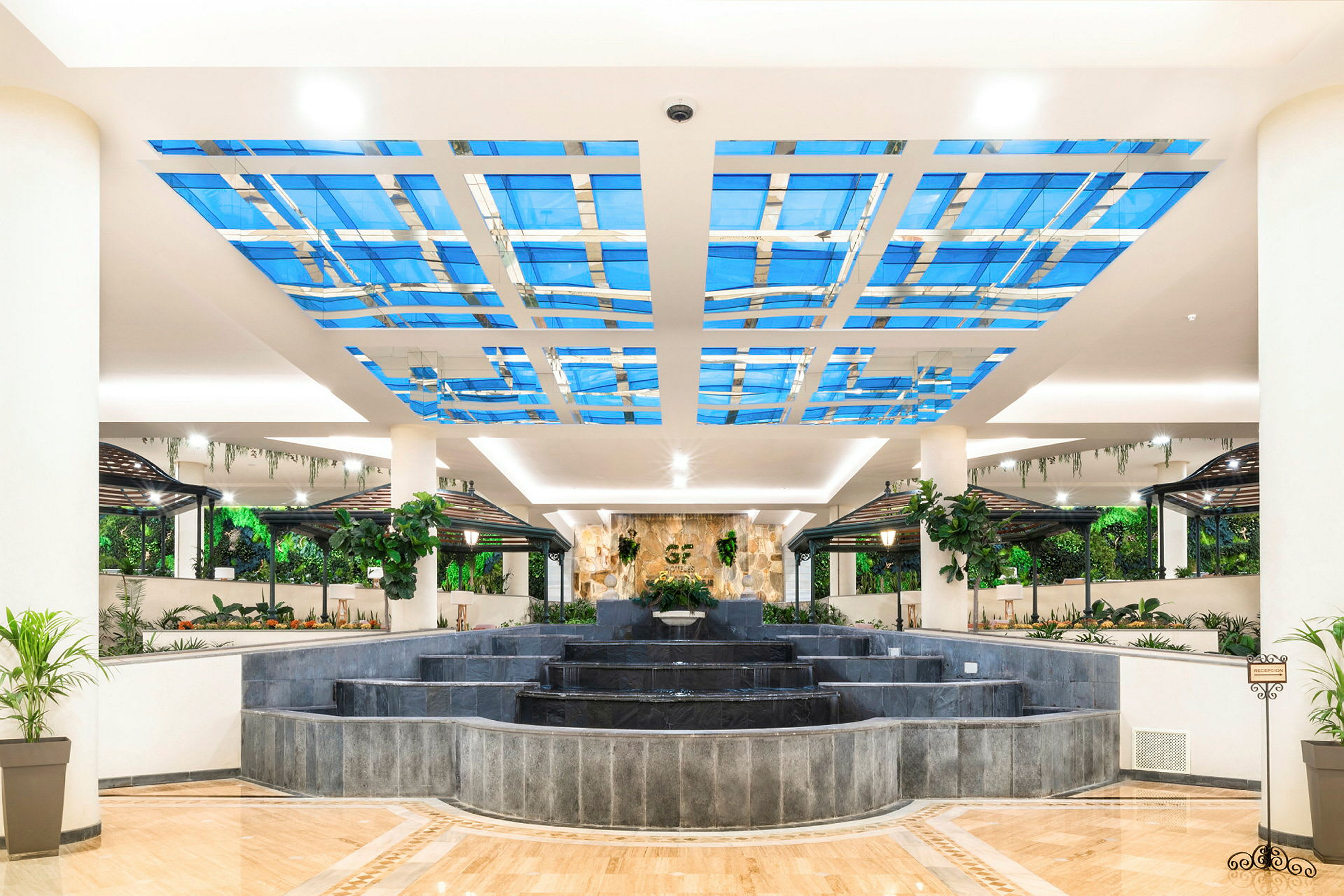 En ljus och öppen hotellobby med fontän och grönskande inredning. (AI-genererad text)