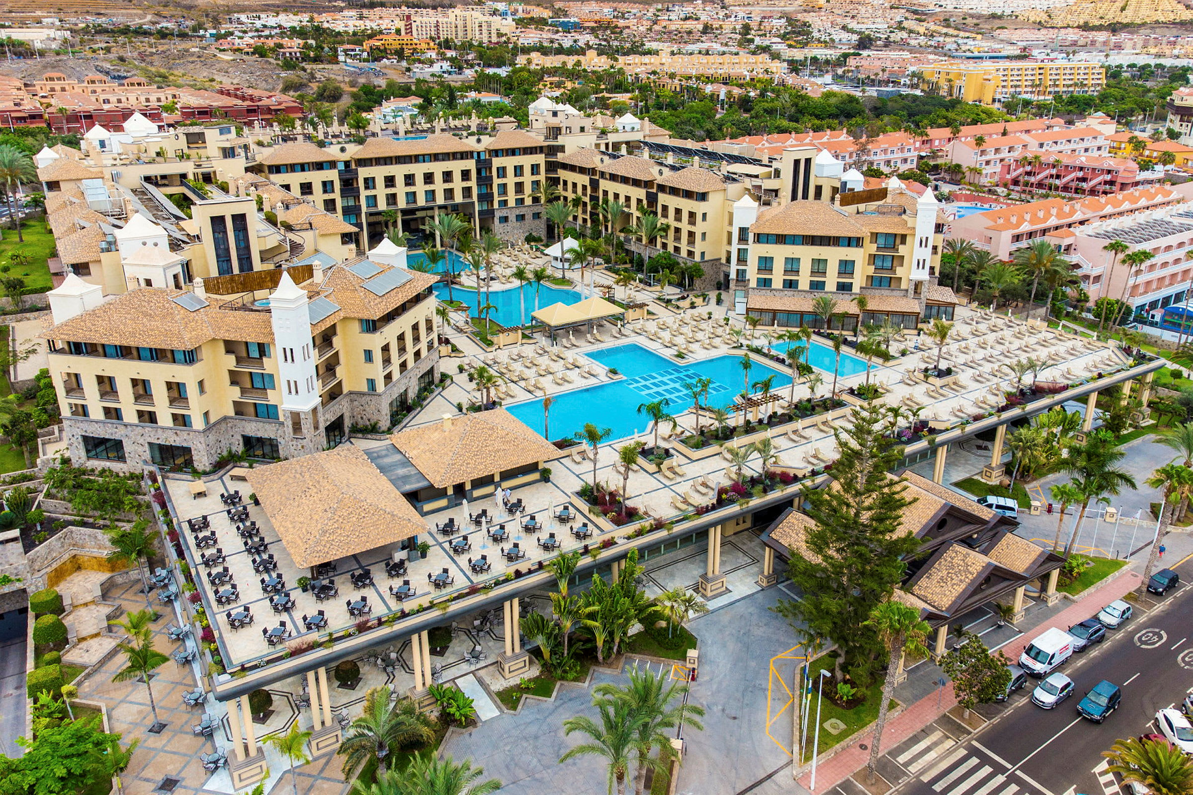 Flygfoto över ett hotellområde med flera byggnader, pooler och solstolar. (AI-genererad text)