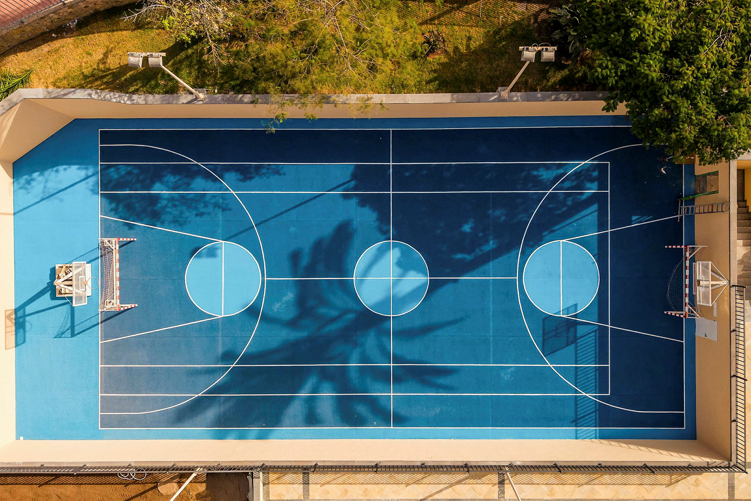 En blå basketplan sedd ovanifrån, med vita linjer och omgiven av träd. (AI-genererad text)