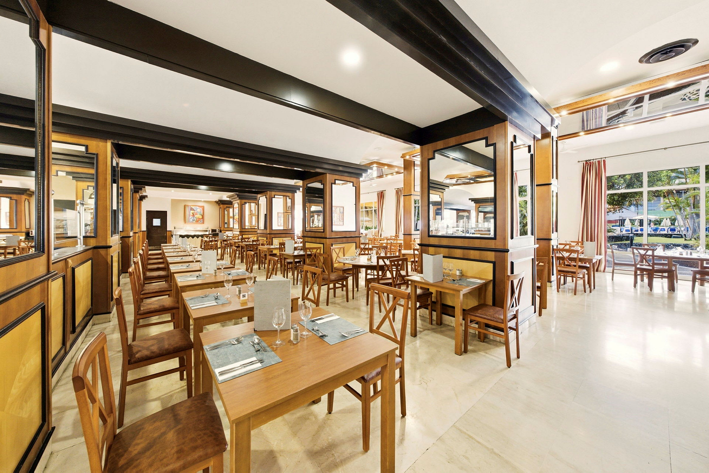 En rymlig restaurang med träbord och stolar, ljus interiör och fönster med utsikt mot träd. (AI-genererad text)