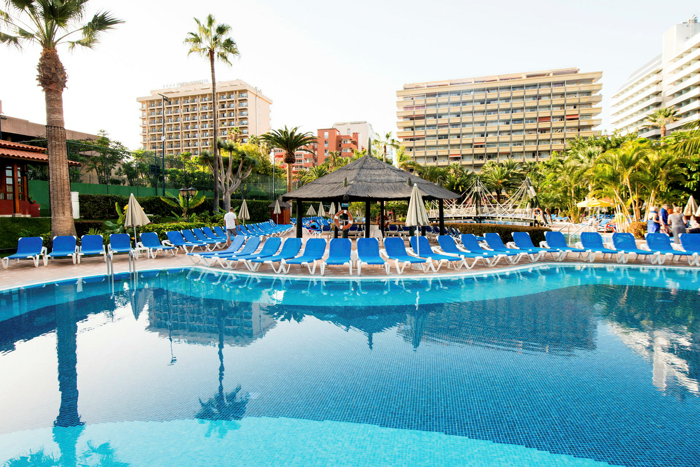 En pool med solstolar runtom och hotellbyggnader i bakgrunden. (AI-genererad text)