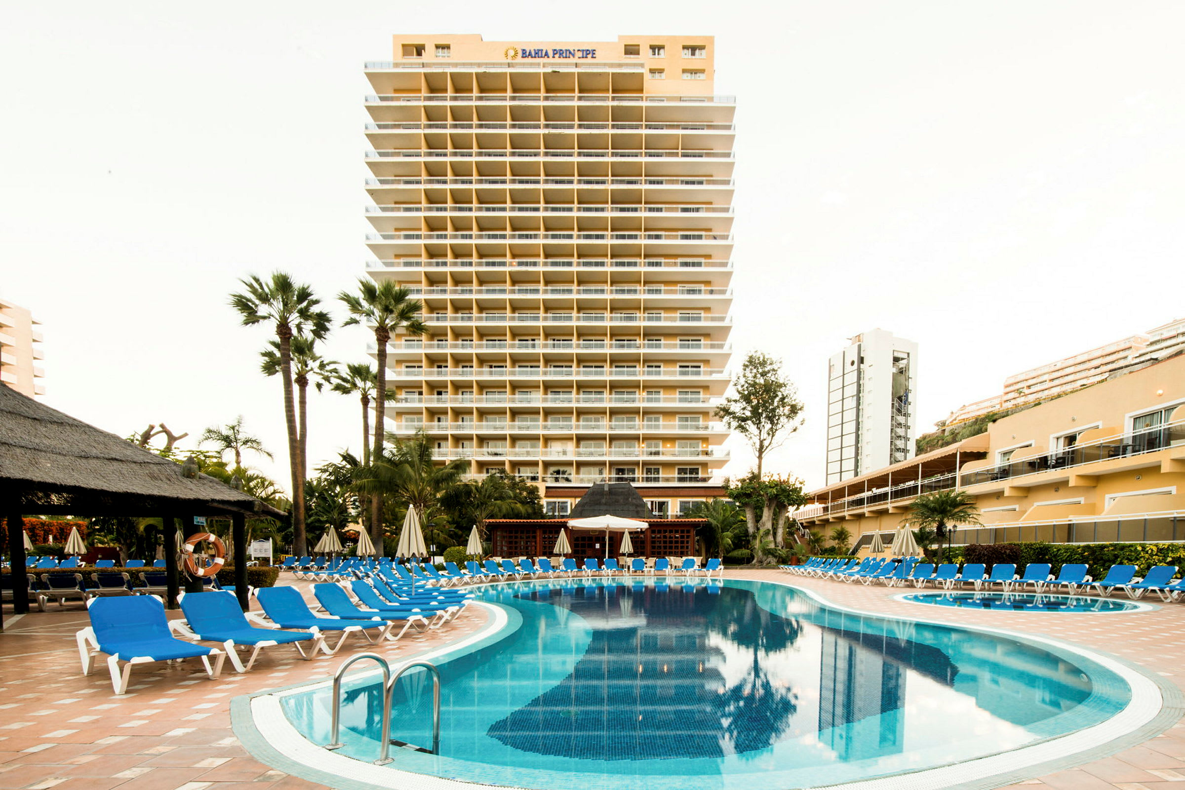 Hotellbyggnad med pool och solstolar framför. (AI-genererad text)