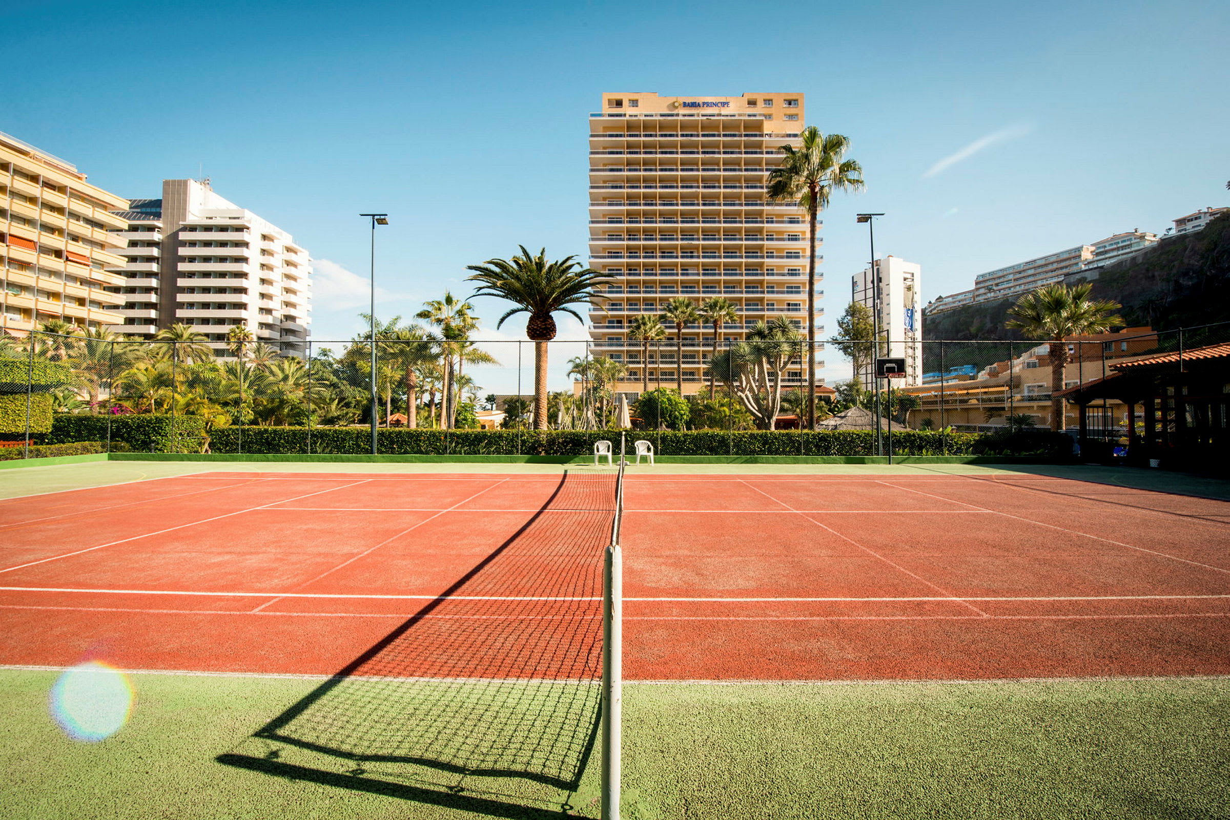 Tennisbana omgiven av palmer och byggnader. (AI-genererad text)