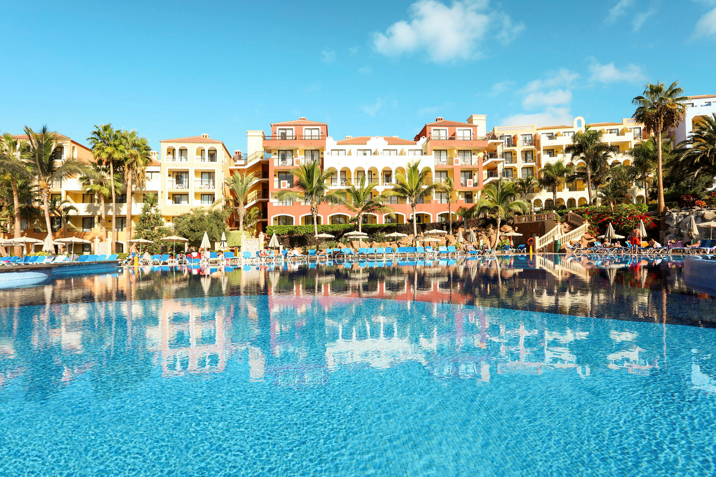 En semesteranläggning med en stor pool och hotellbyggnader i bakgrunden. (AI-genererad text)