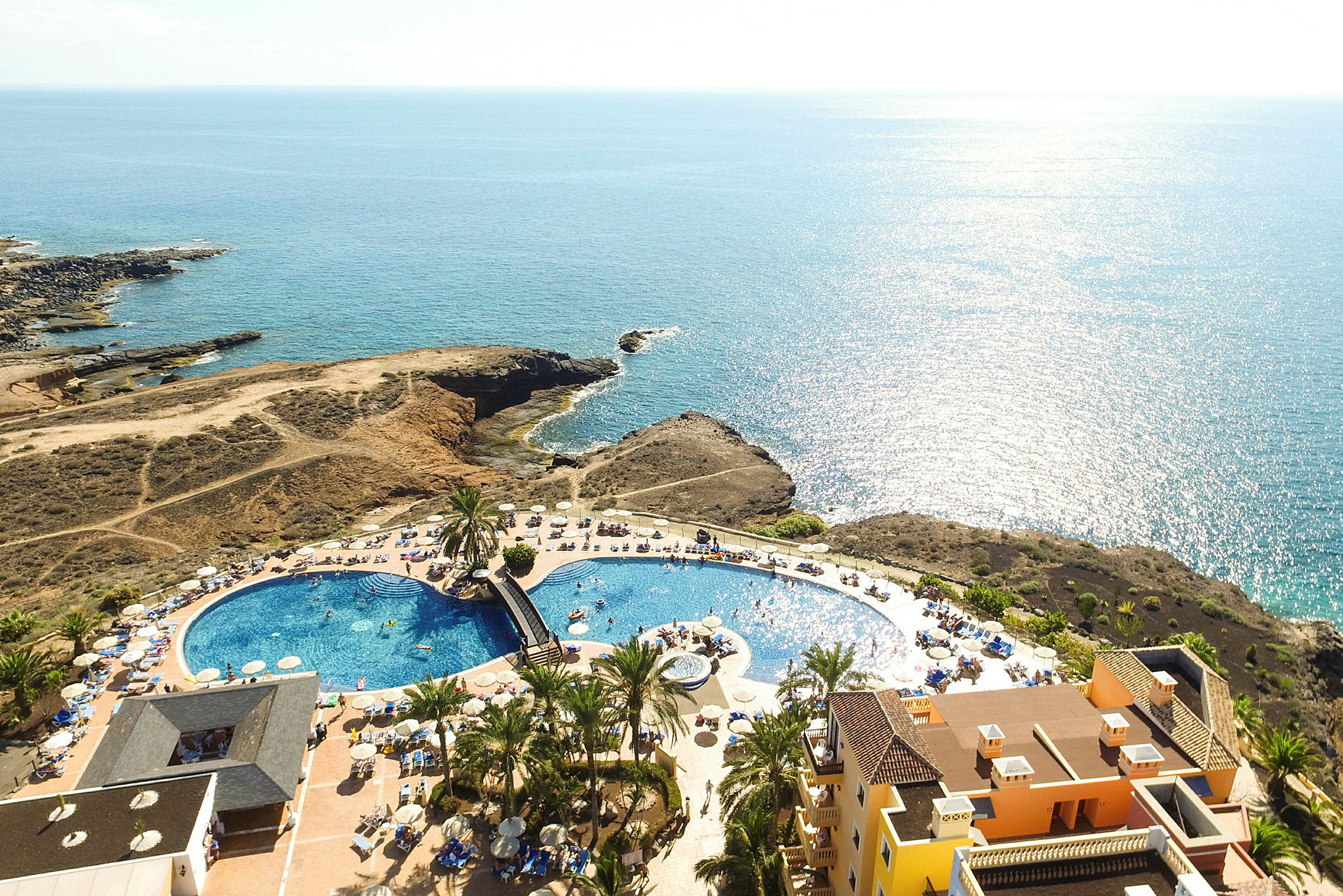 Flygbild av en resort med pool, solstolar och havsutsikt. (AI-genererad text)