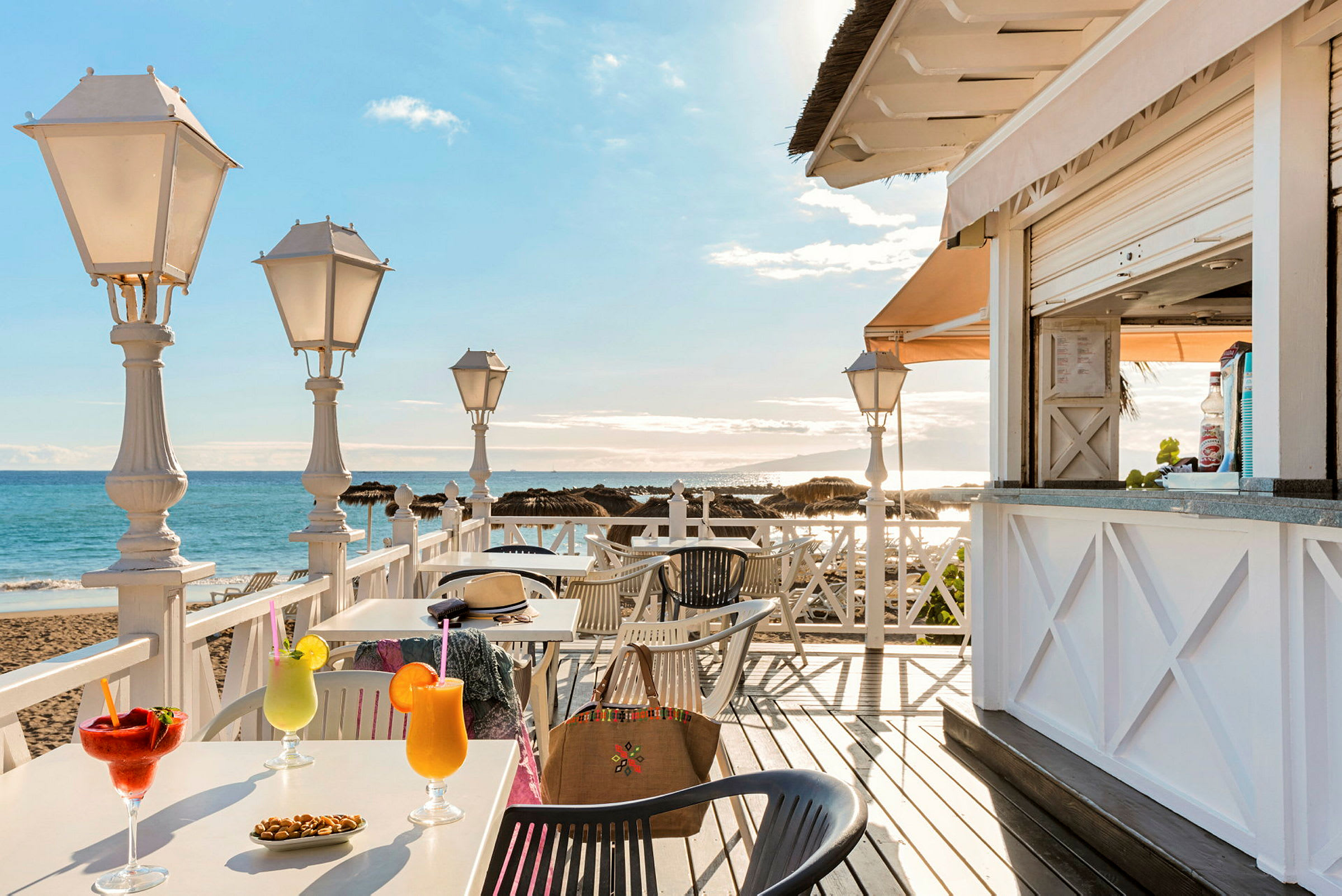 En strandcafeteria med bord, drinkar och utsikt över havet. (AI-genererad text)