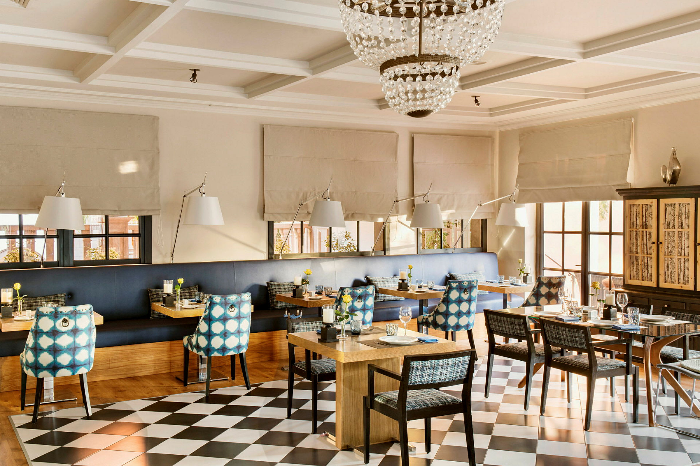 En inomhusrestaurang med dukade bord, stolar med mönstrade ryggstöd och en kristallkrona i taket. (AI-genererad text)