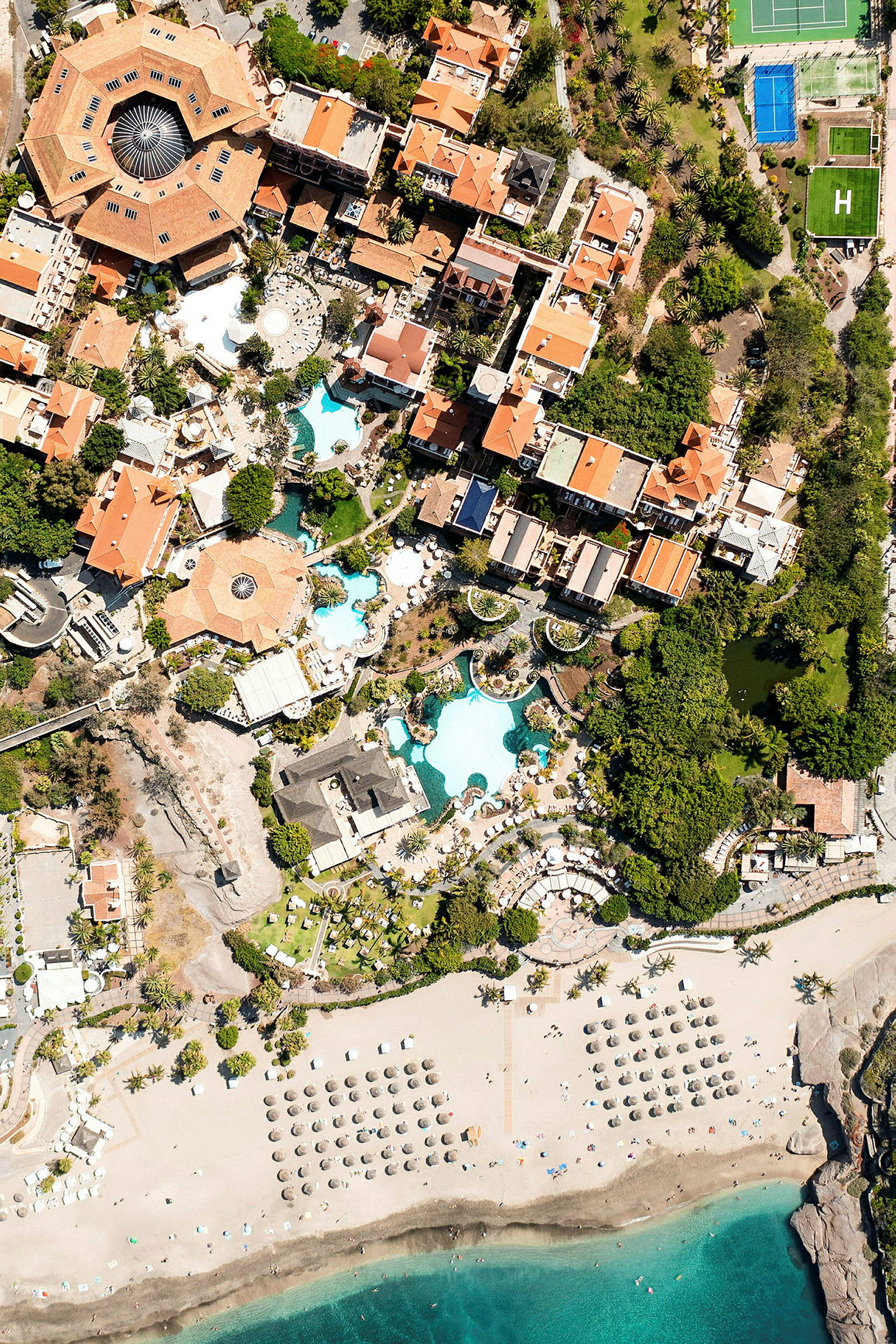 Flygfoto av en semesterort med byggnader, swimmingpooler och sandstrand. (AI-genererad text)