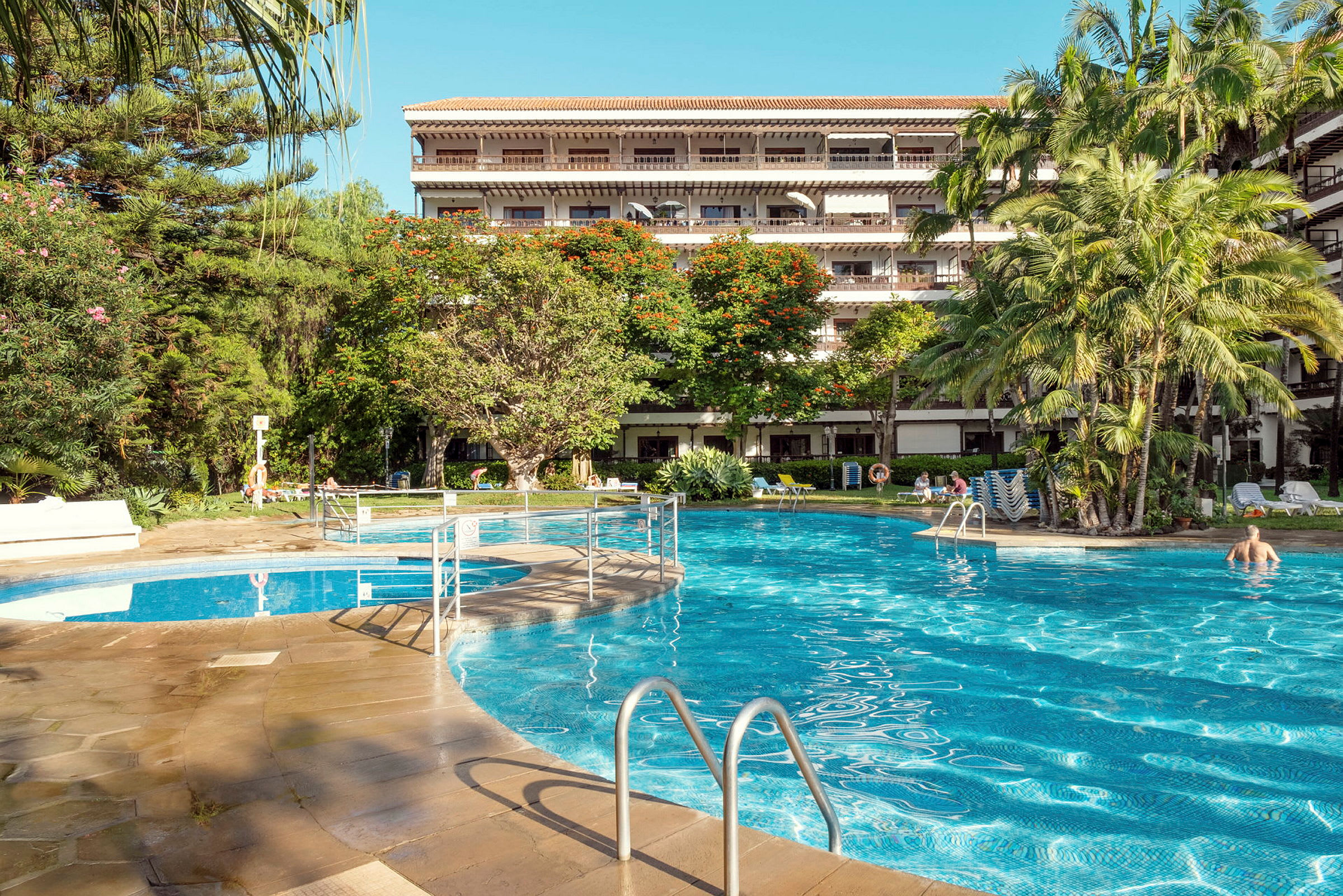 Utomhuspool vid hotell omgivet av grönska. (AI-genererad text)