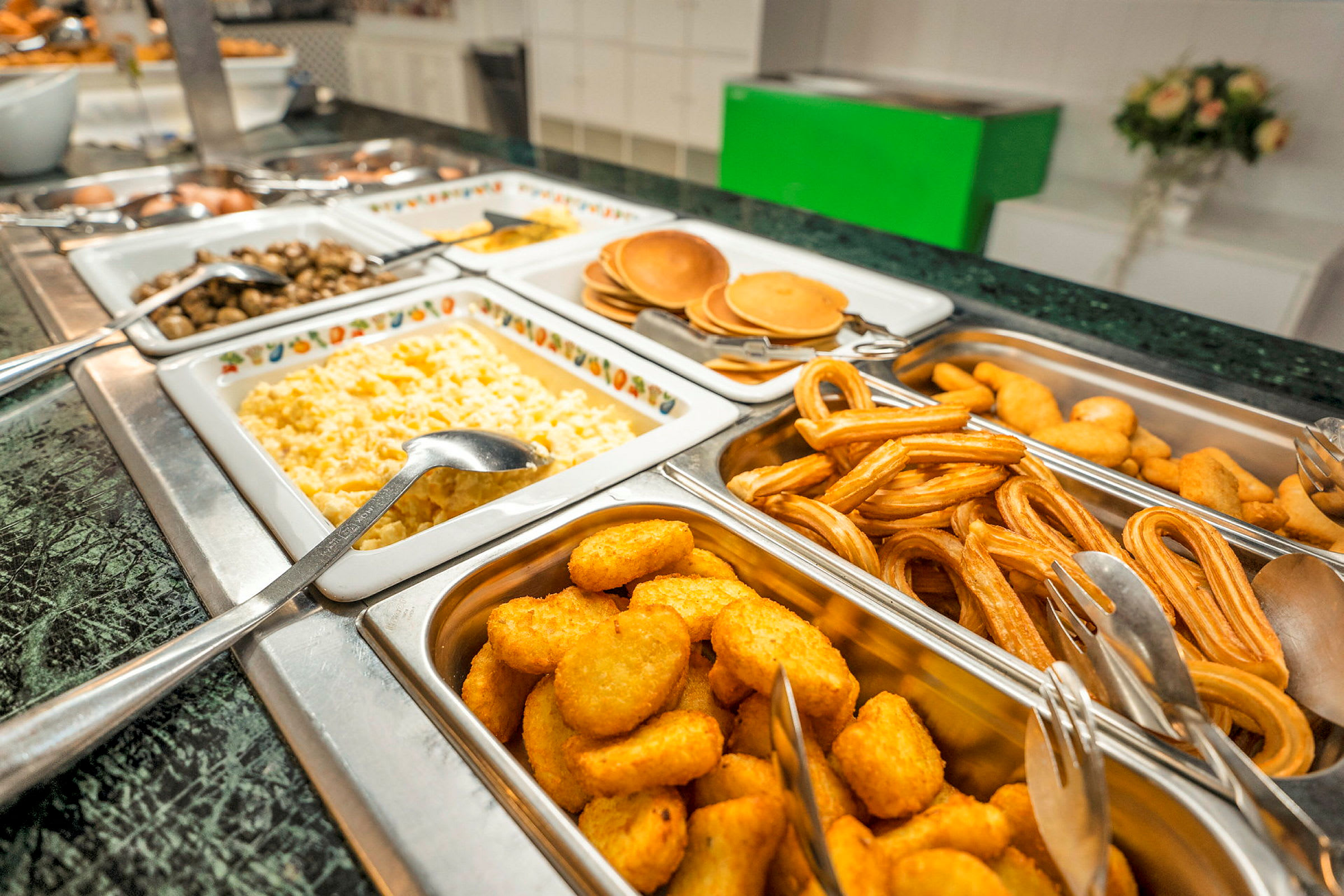 Bild på en buffé fylld med olika maträtter, inklusive äggröra, pannkakor, churros och gyllene nuggets. (AI-genererad text)