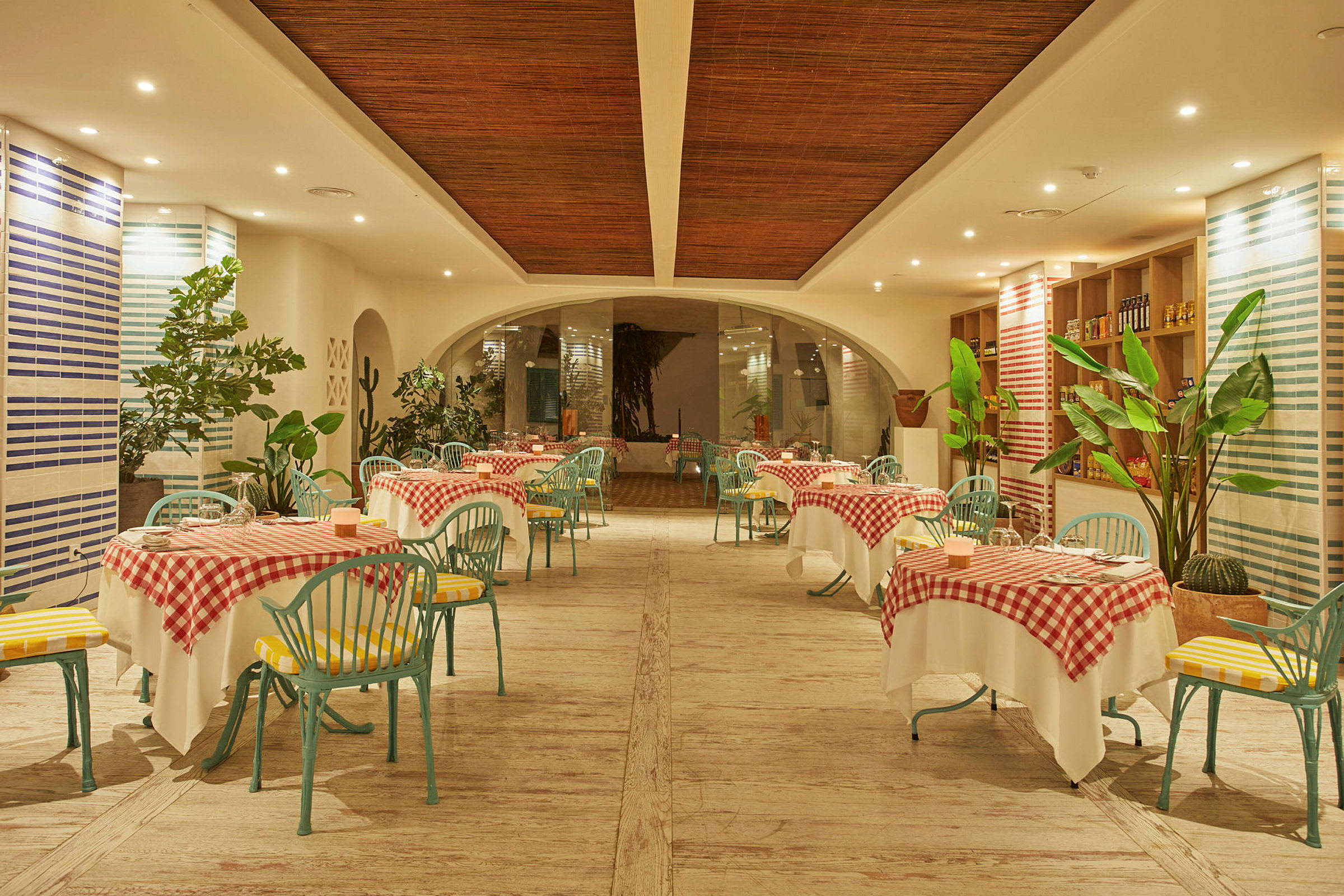 En restaurang med bord klädda i rödrutiga dukar och gröna stolar, omgiven av växter. (AI-genererad text)