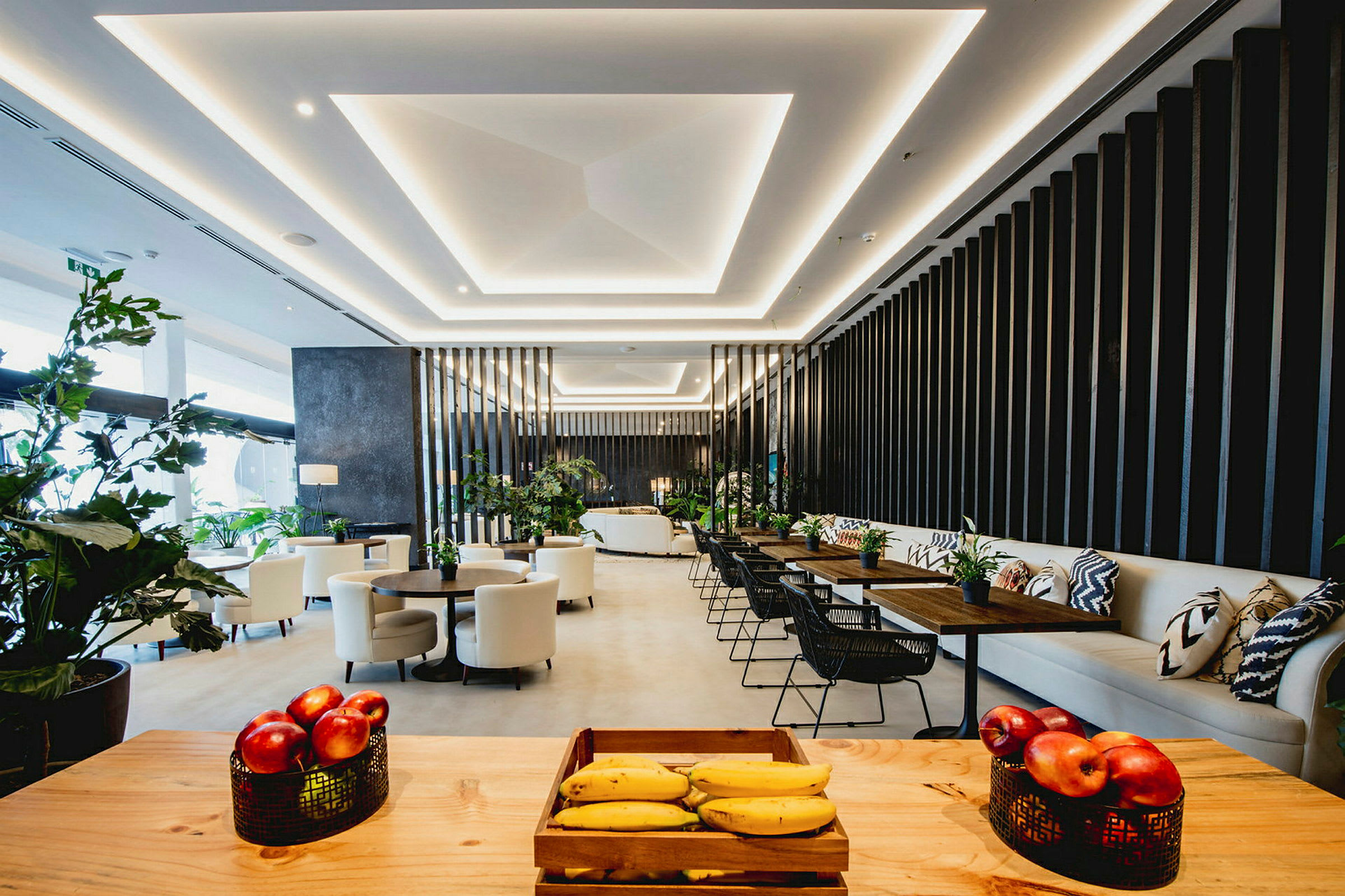 En modern lounge med sittgrupper, dekorativa växter och en fruktskål på ett bord i förgrunden. (AI-genererad text)