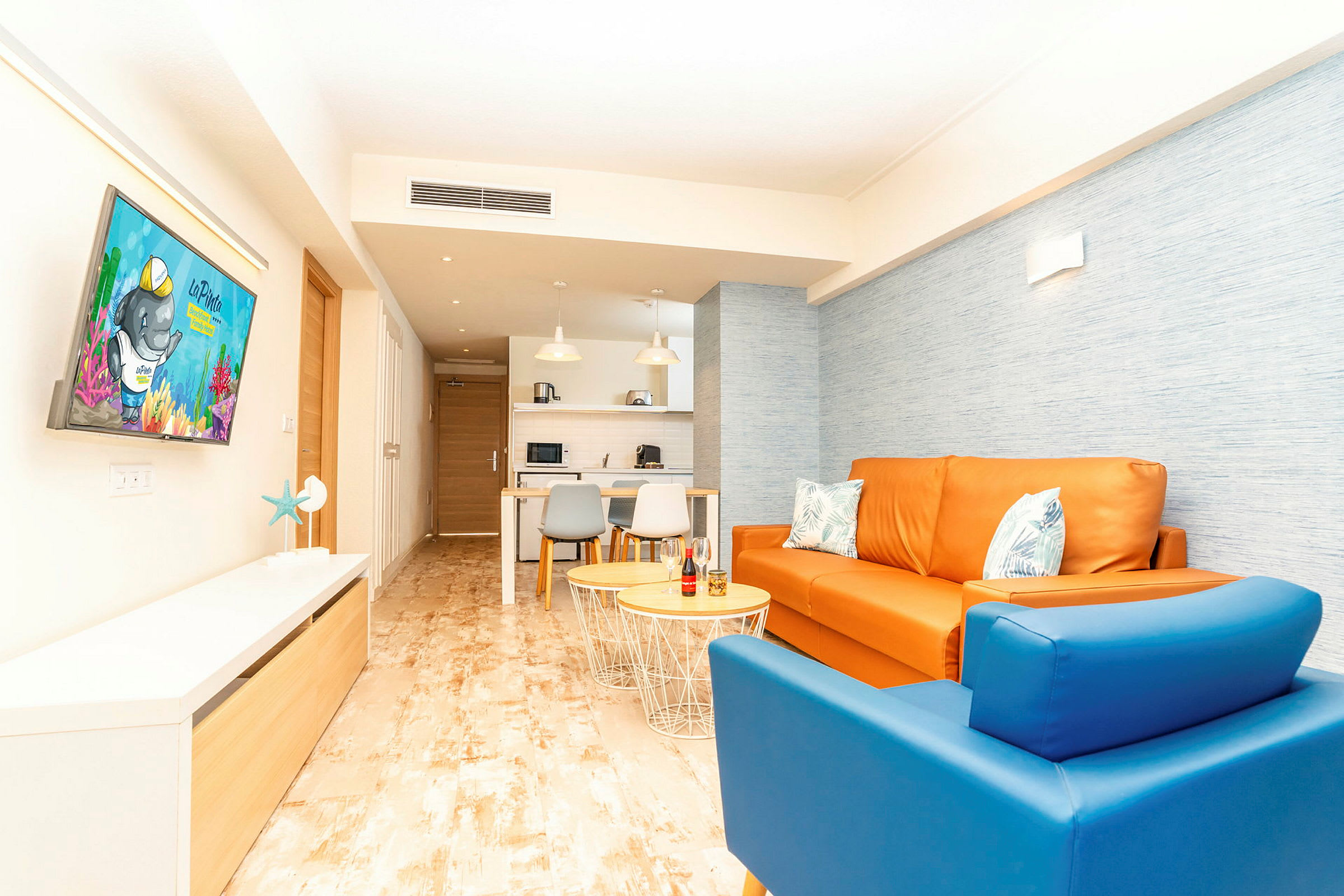 Ett färgglatt vardagsrum med orange soffa och blå fåtölj, synligt från kök till tv. (AI-genererad text)