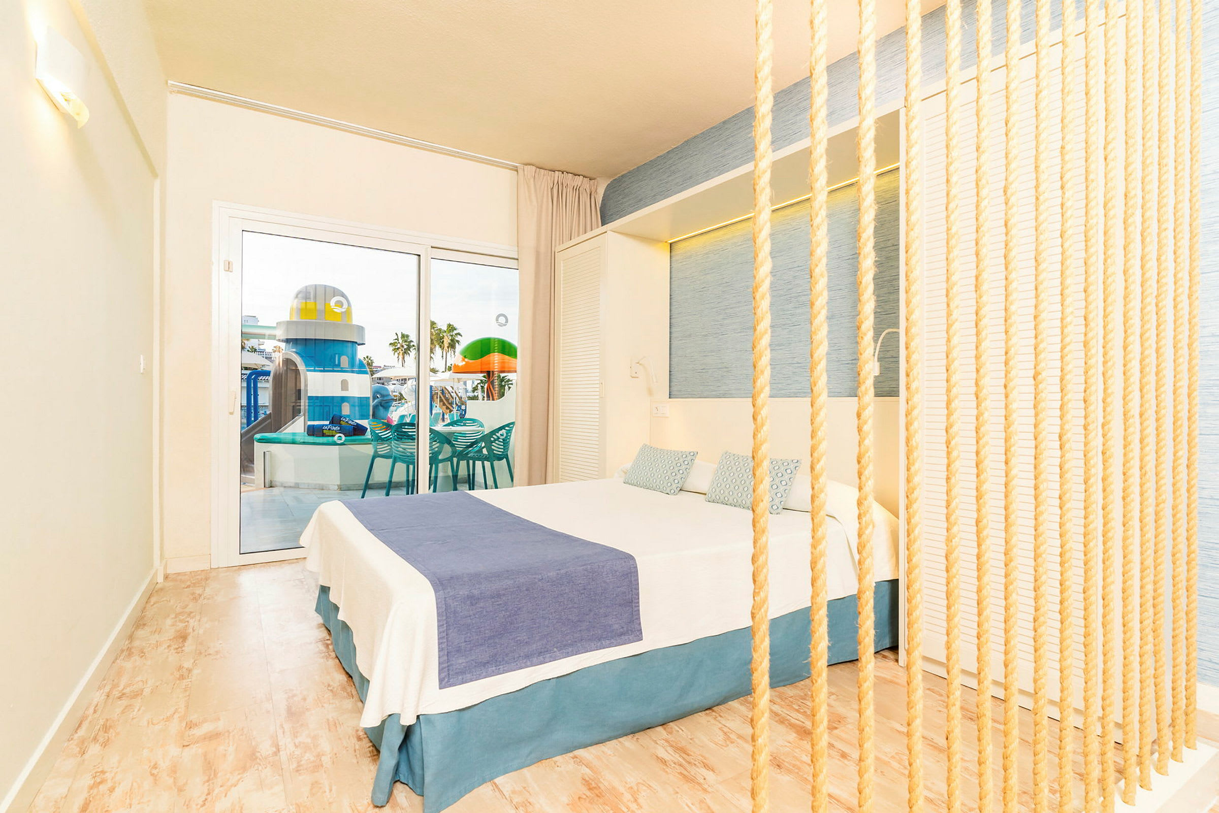 Hotellrum med ljus inredning och utsikt mot en pool och lekplats. (AI-genererad text)