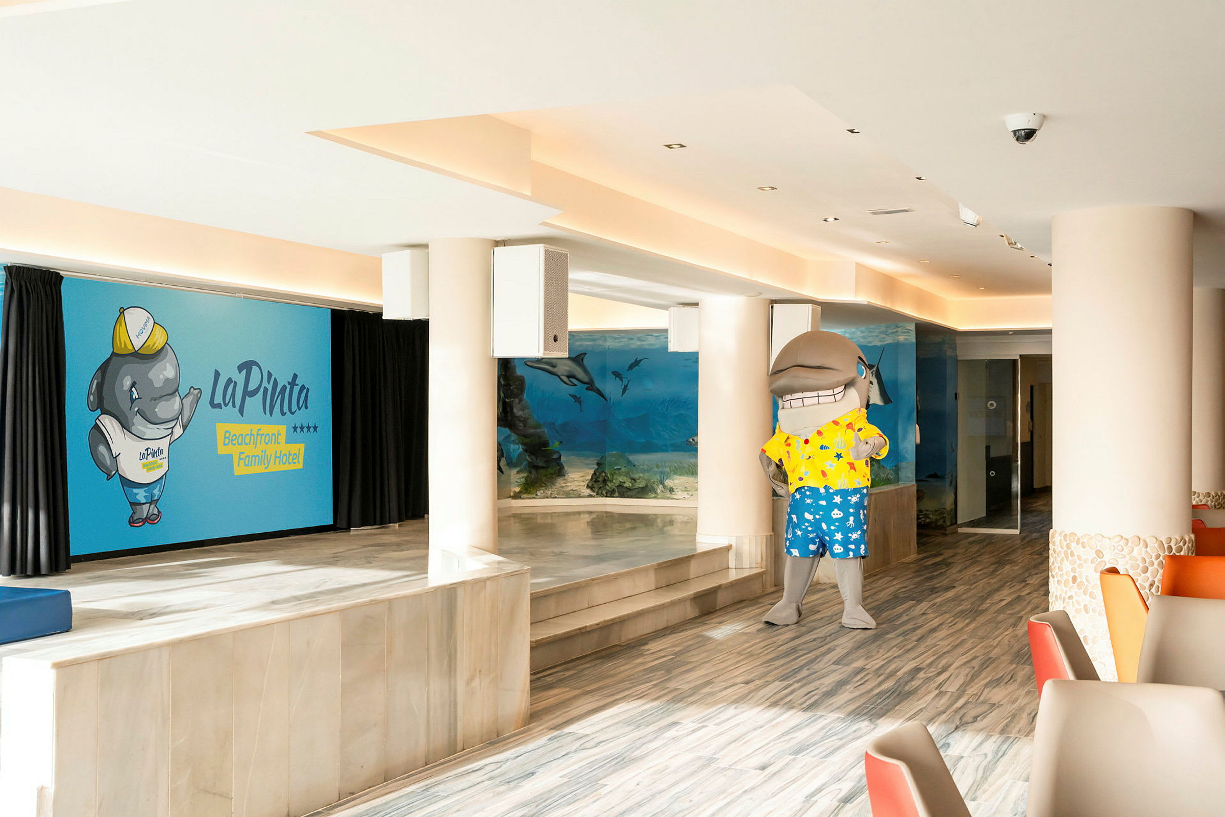 En hotellinteriör med en akvariumvägg och en delfinmaskot. (AI-genererad text)